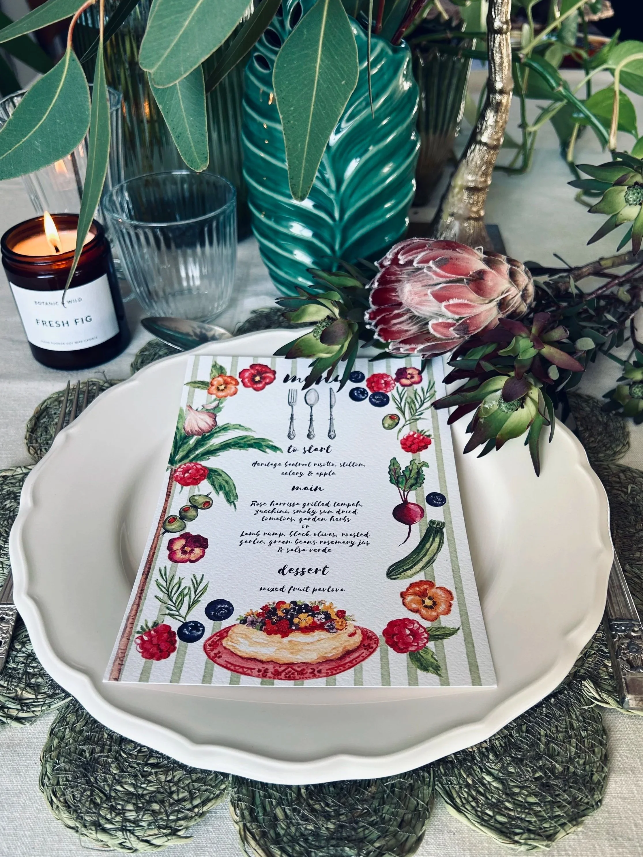 A coastal-themed table setting with a menu featuring seafood dishes, decorated with seashells, starfish, and greenery, set on a woven placemat with flowers and glassware nearby.