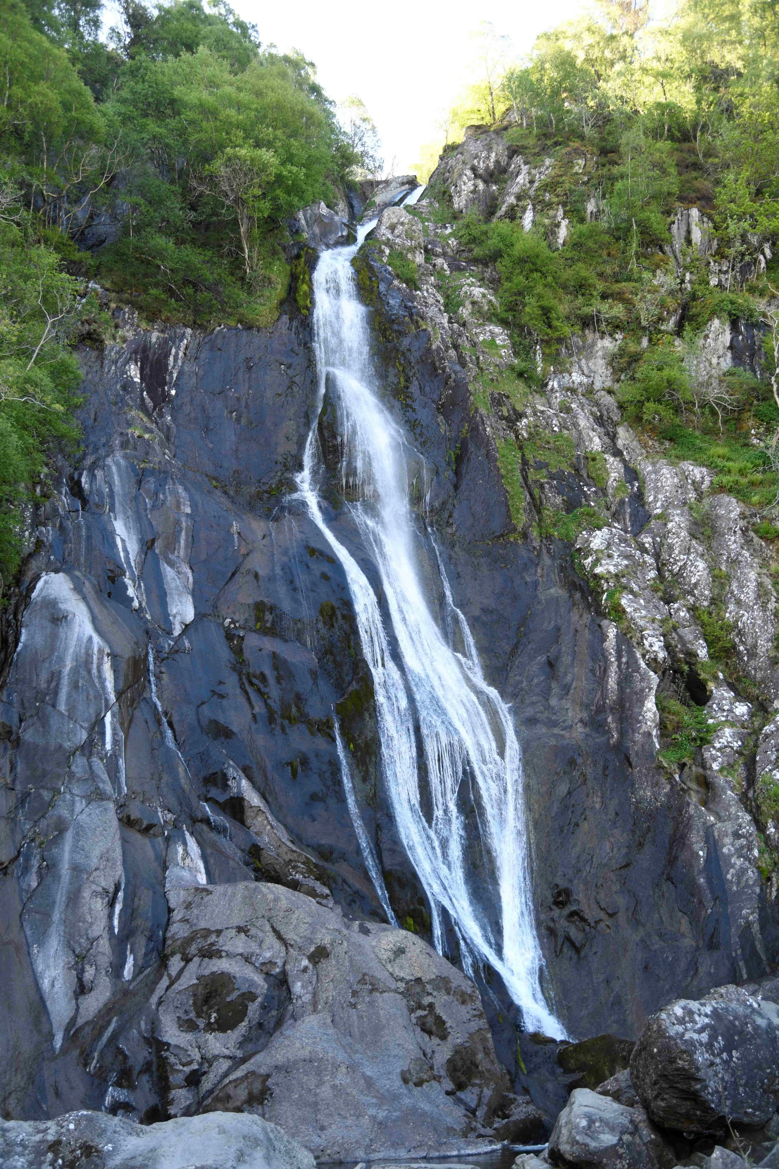 A tall waterfall cascading down a rocky cliff surrounded by green trees and vegetation.