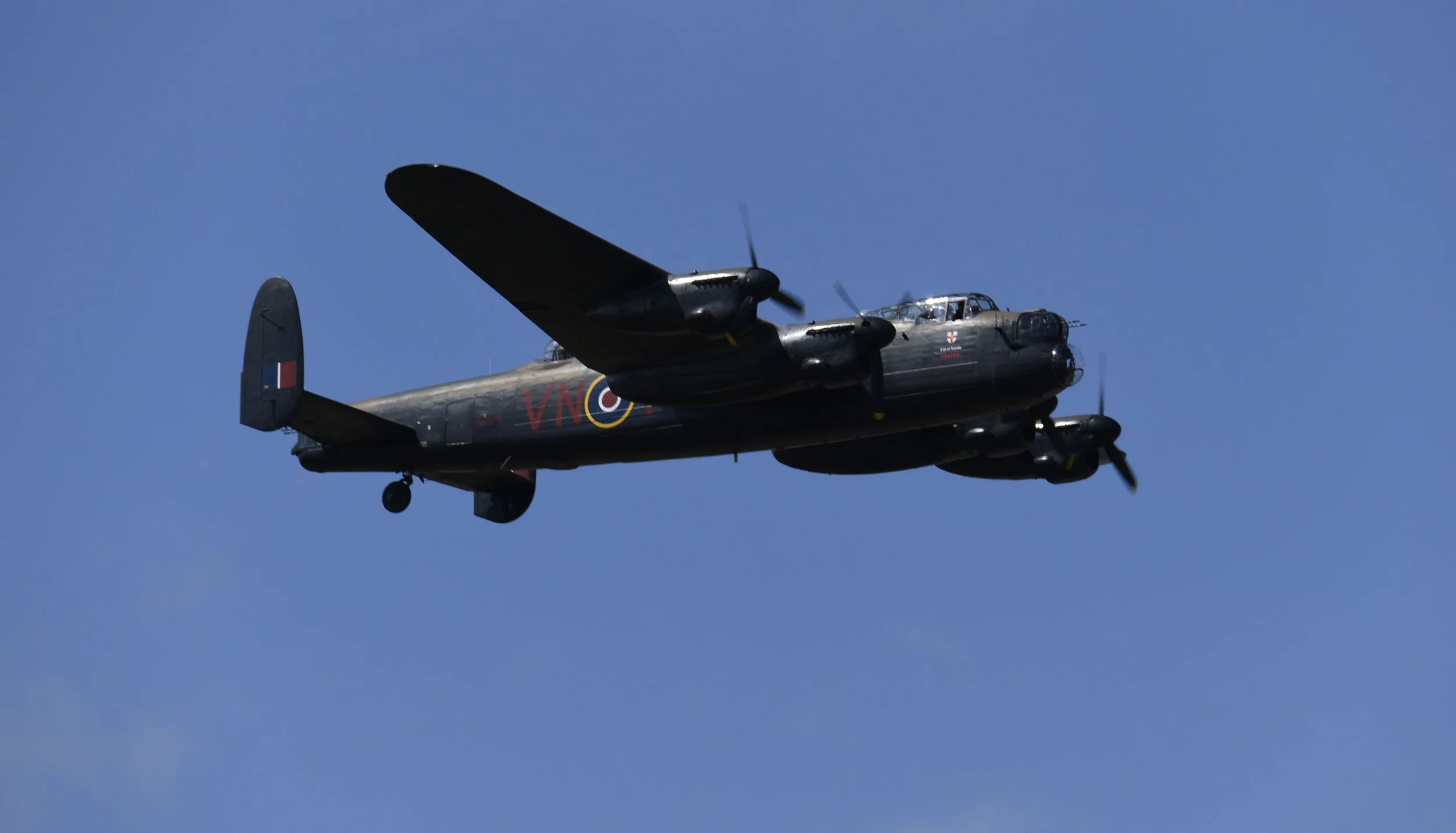 A black military aircraft flying in a clear blue sky.