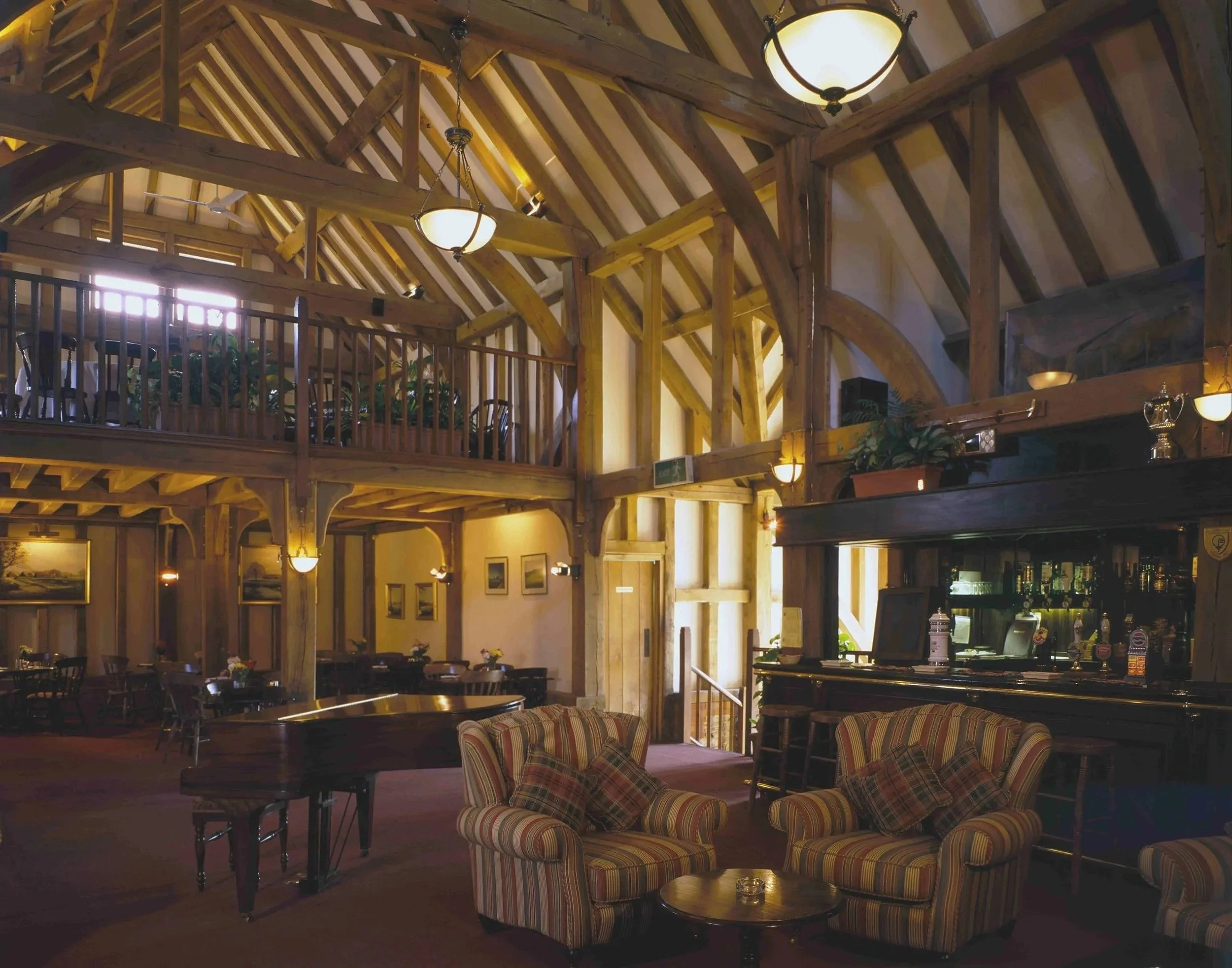 Interior of a rustic restaurant or pub with wooden beams, hanging lights, tables, and chairs. Decorations include framed pictures and plants.