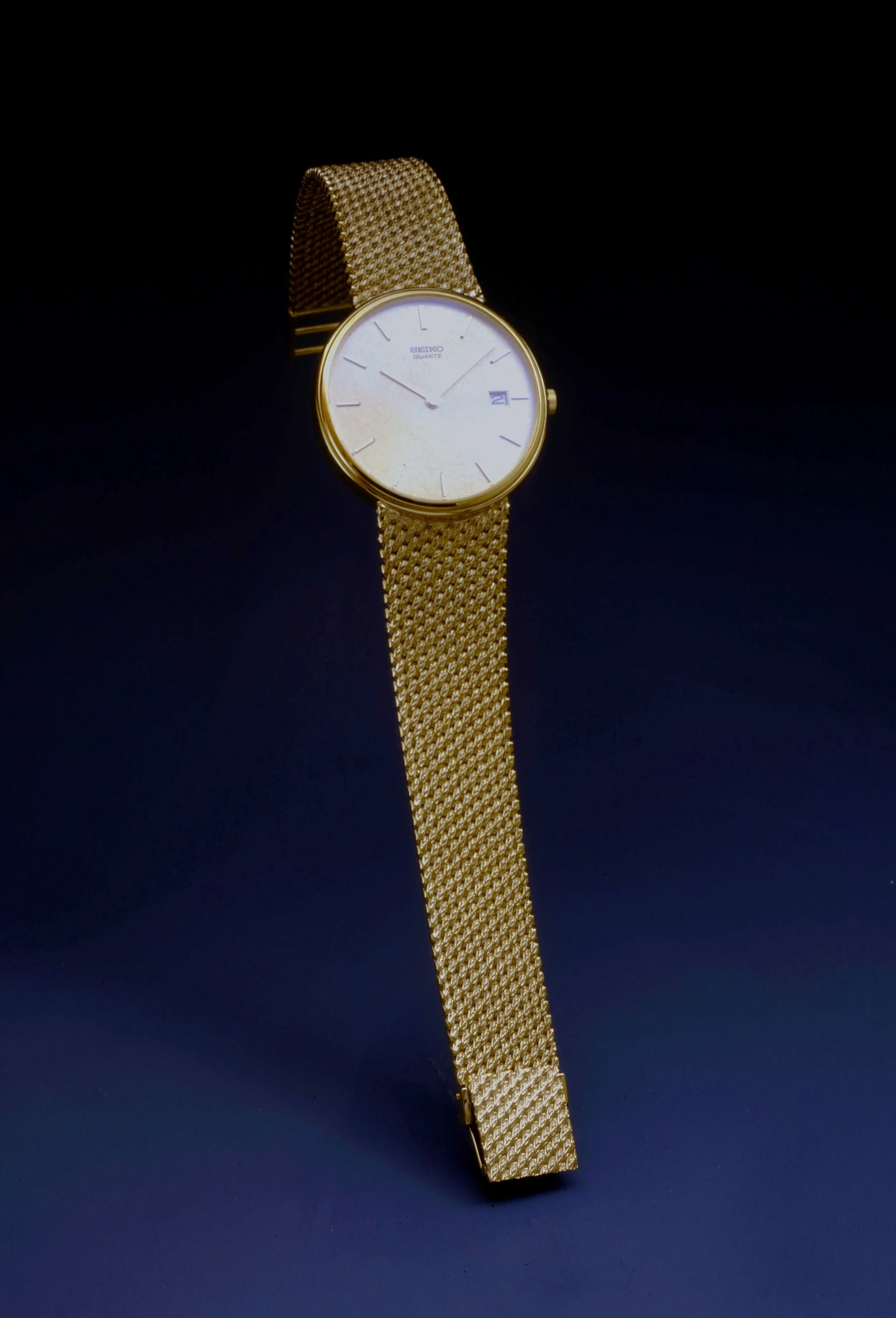 Gold Seiko quartz wristwatch with a mesh band and a white face showing the time and date.