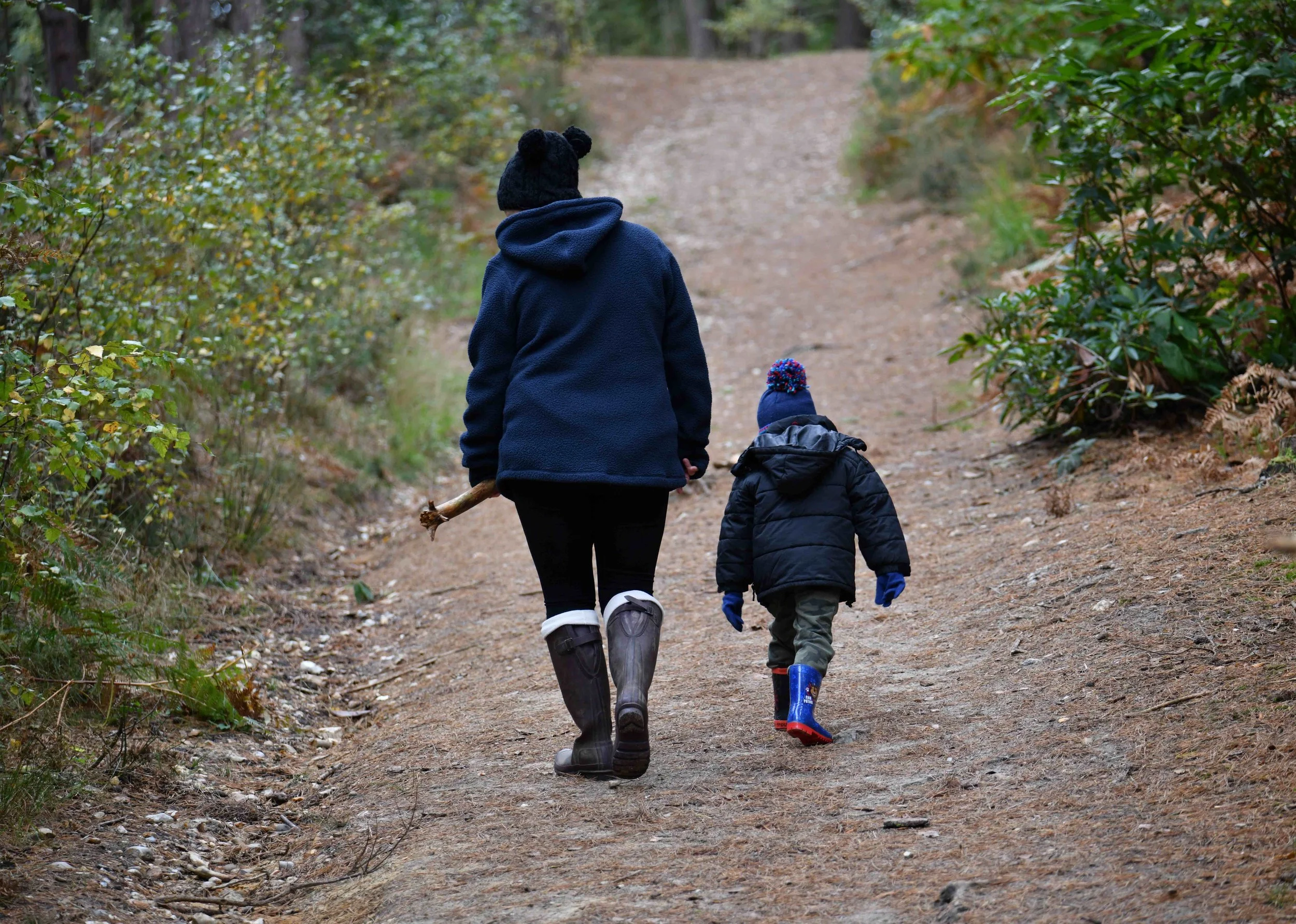 Two children walking on a trail in the woods, wearing winter clothing and boots.