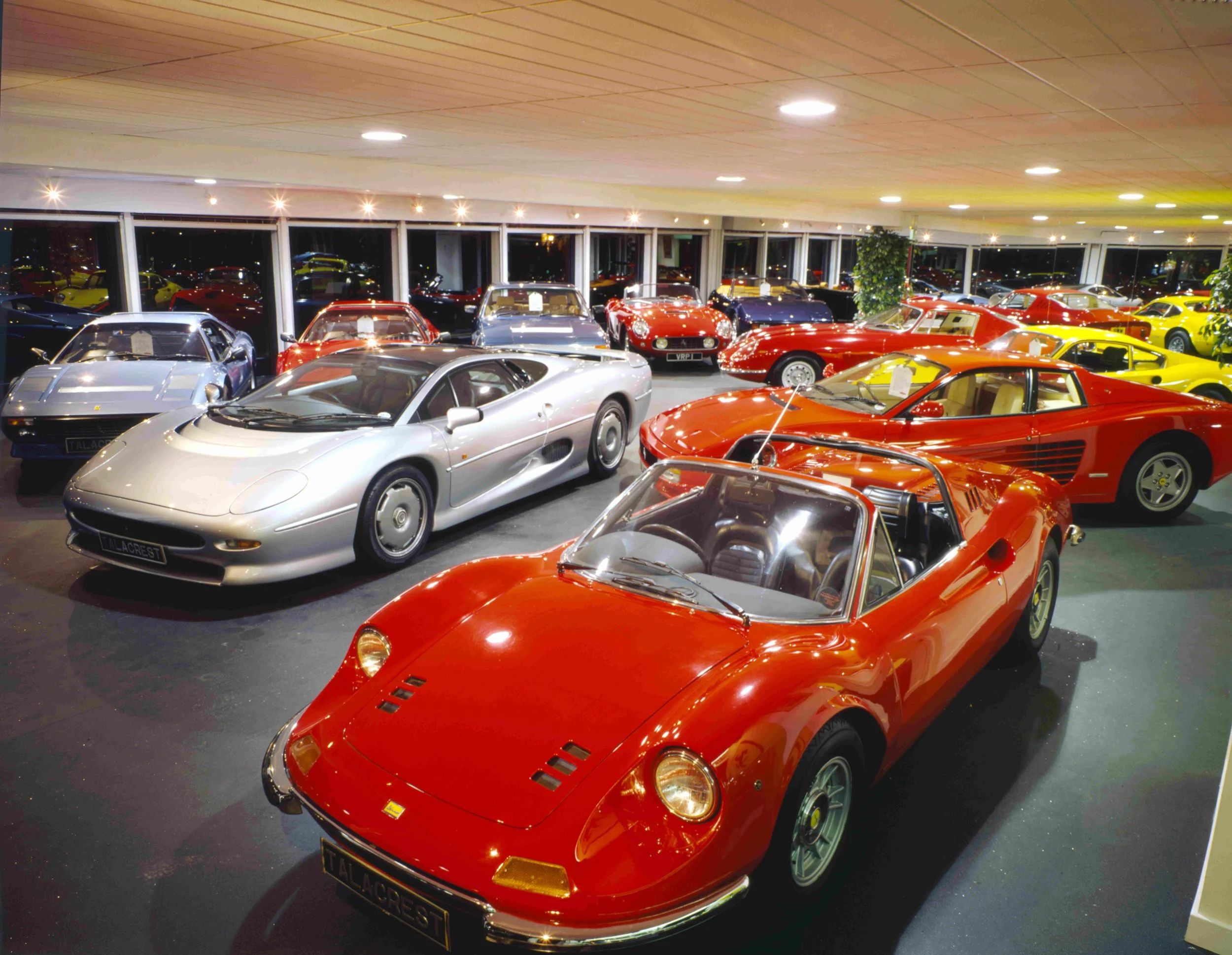 A collection of classic cars in a showroom, with many sports cars including red, yellow, and silver models displayed indoors.