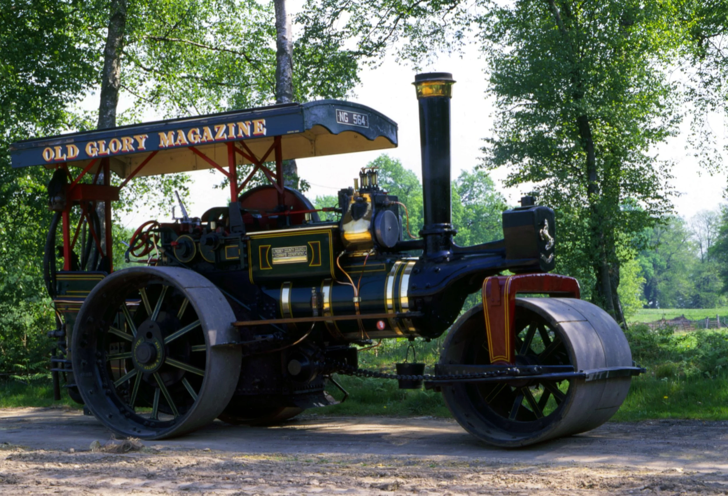 An antique steam-powered traction engine outdoors on grass, with green trees in the background.