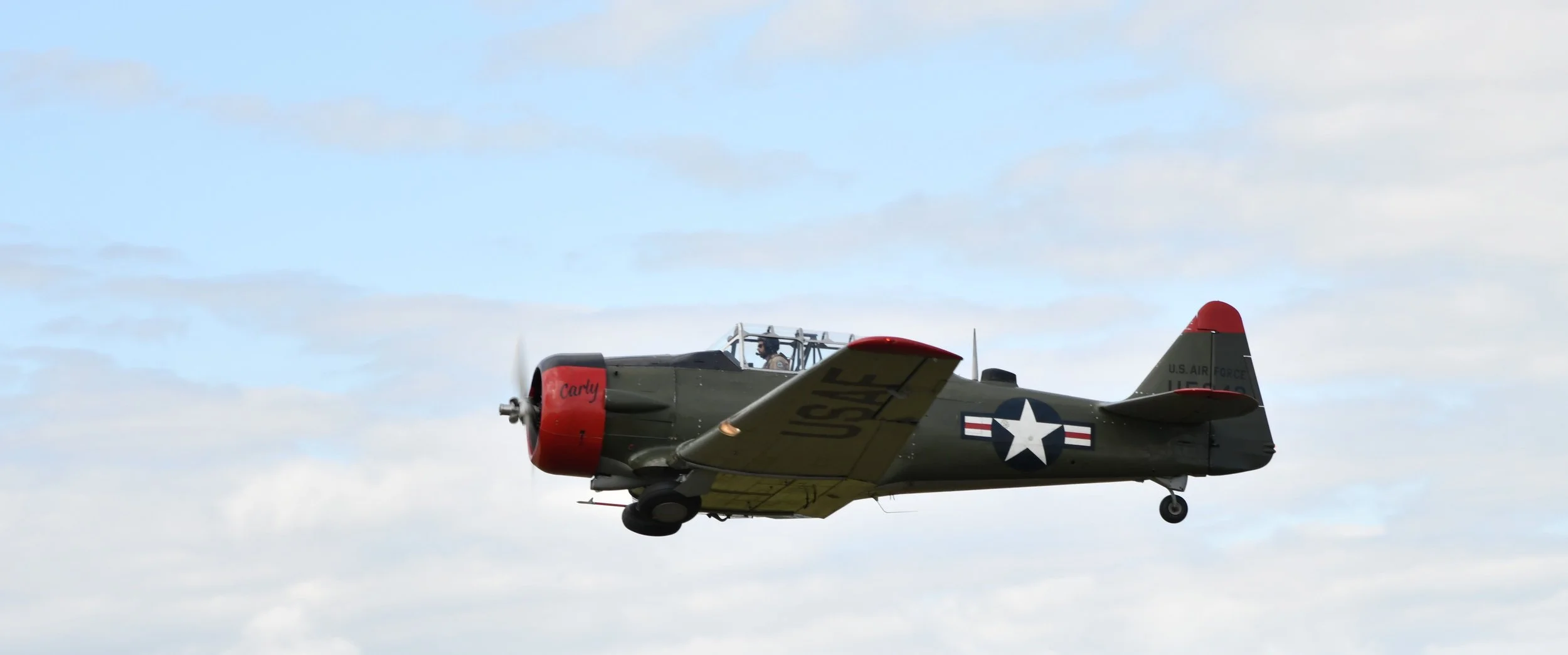 A vintage military aircraft flying in the sky with clouds.