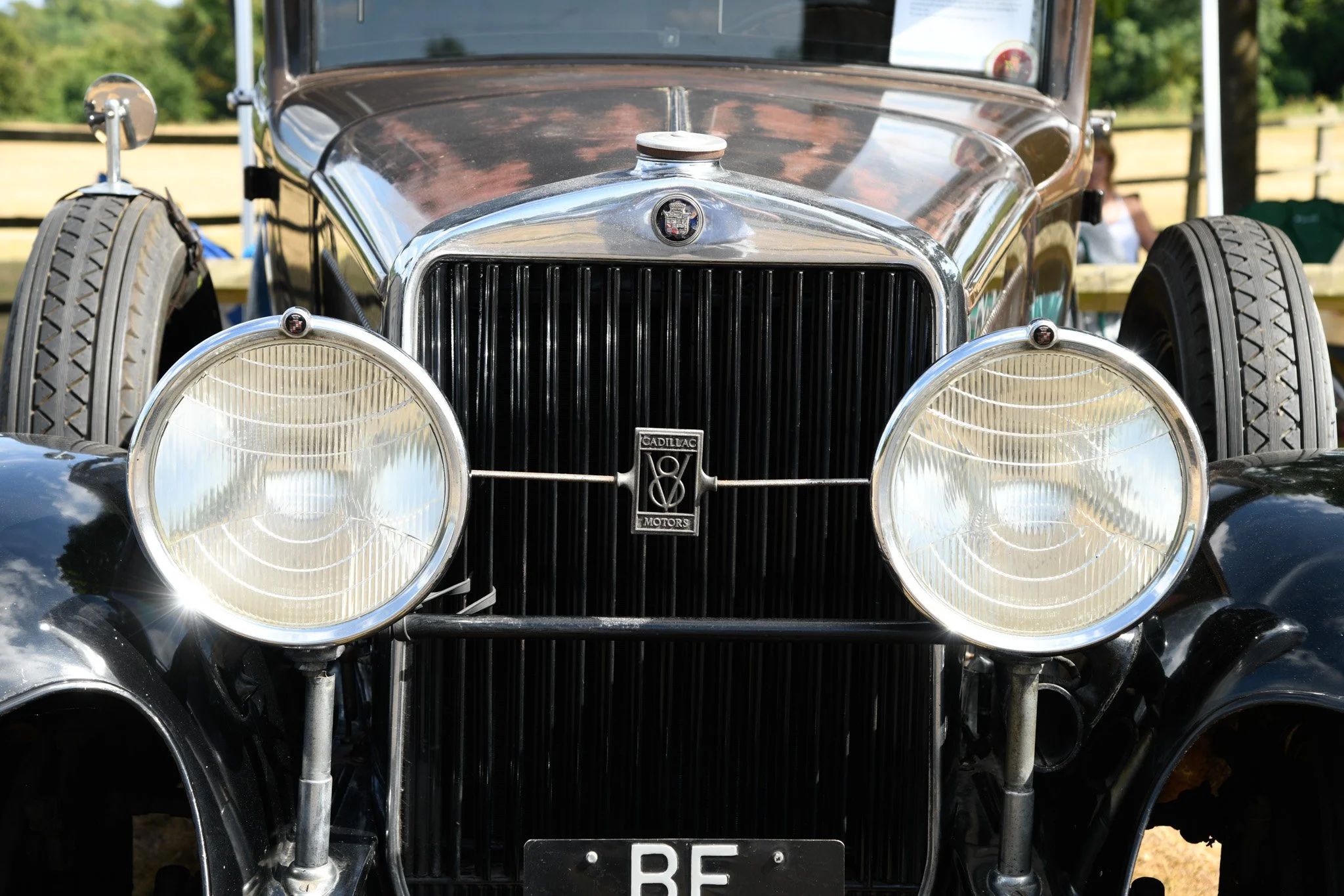 Front view of a vintage black Cadillac car with round headlights and a chrome grille, parked outdoors on a sunny day.