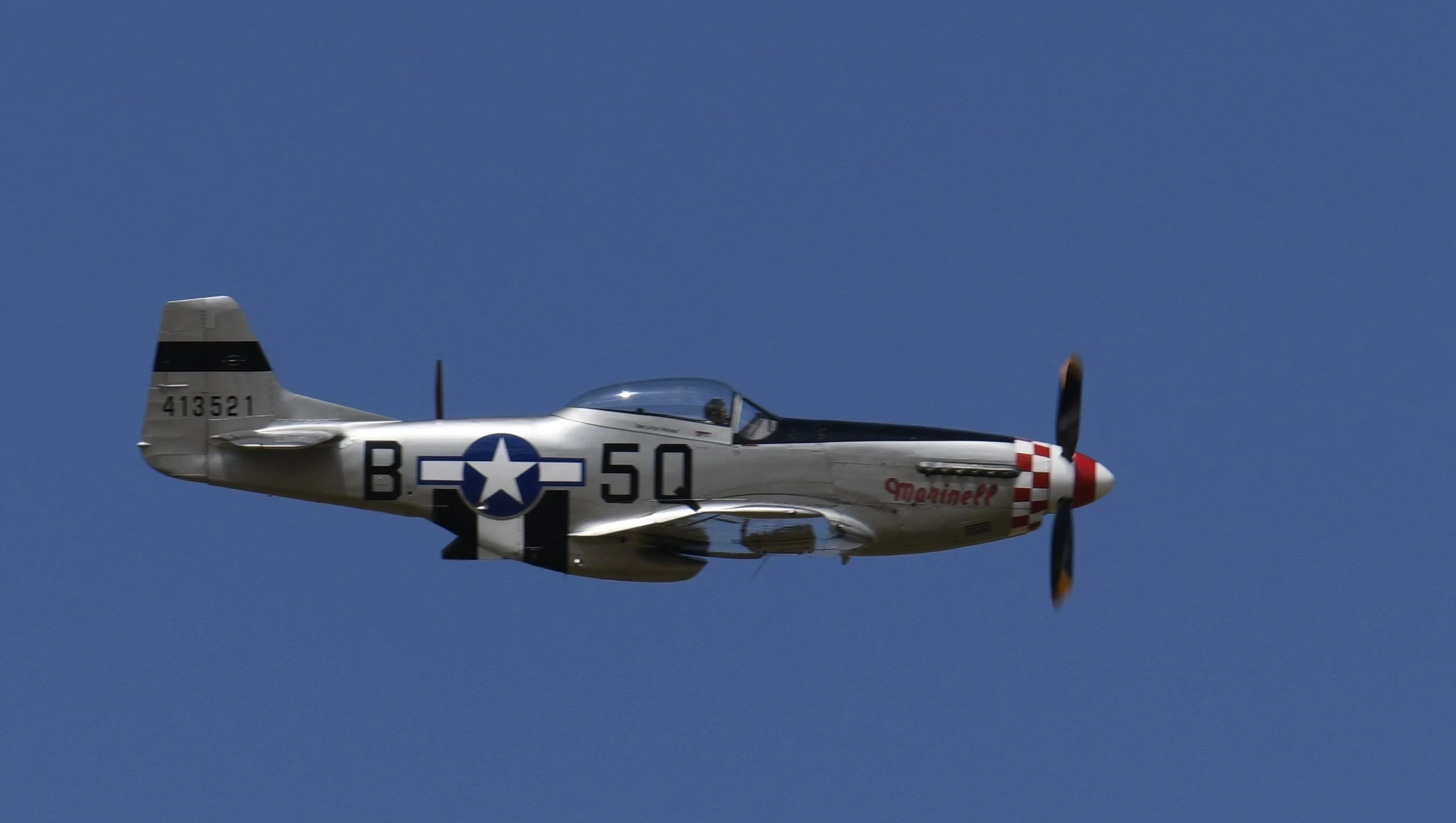 A vintage silver military aircraft with a propeller flying against a clear blue sky.