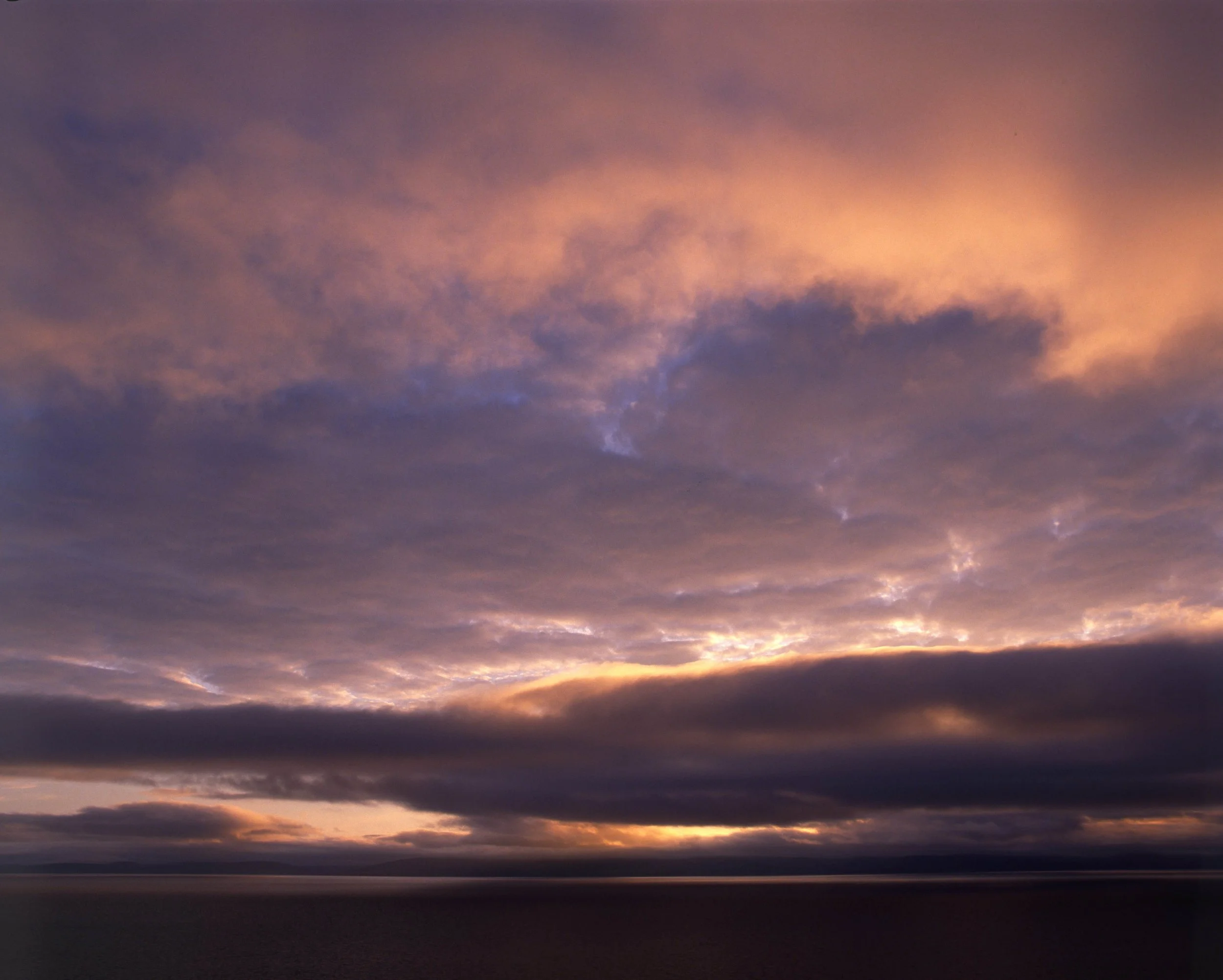 A scenic view of a sunset sky with pink, purple, and orange clouds over a dark horizon.