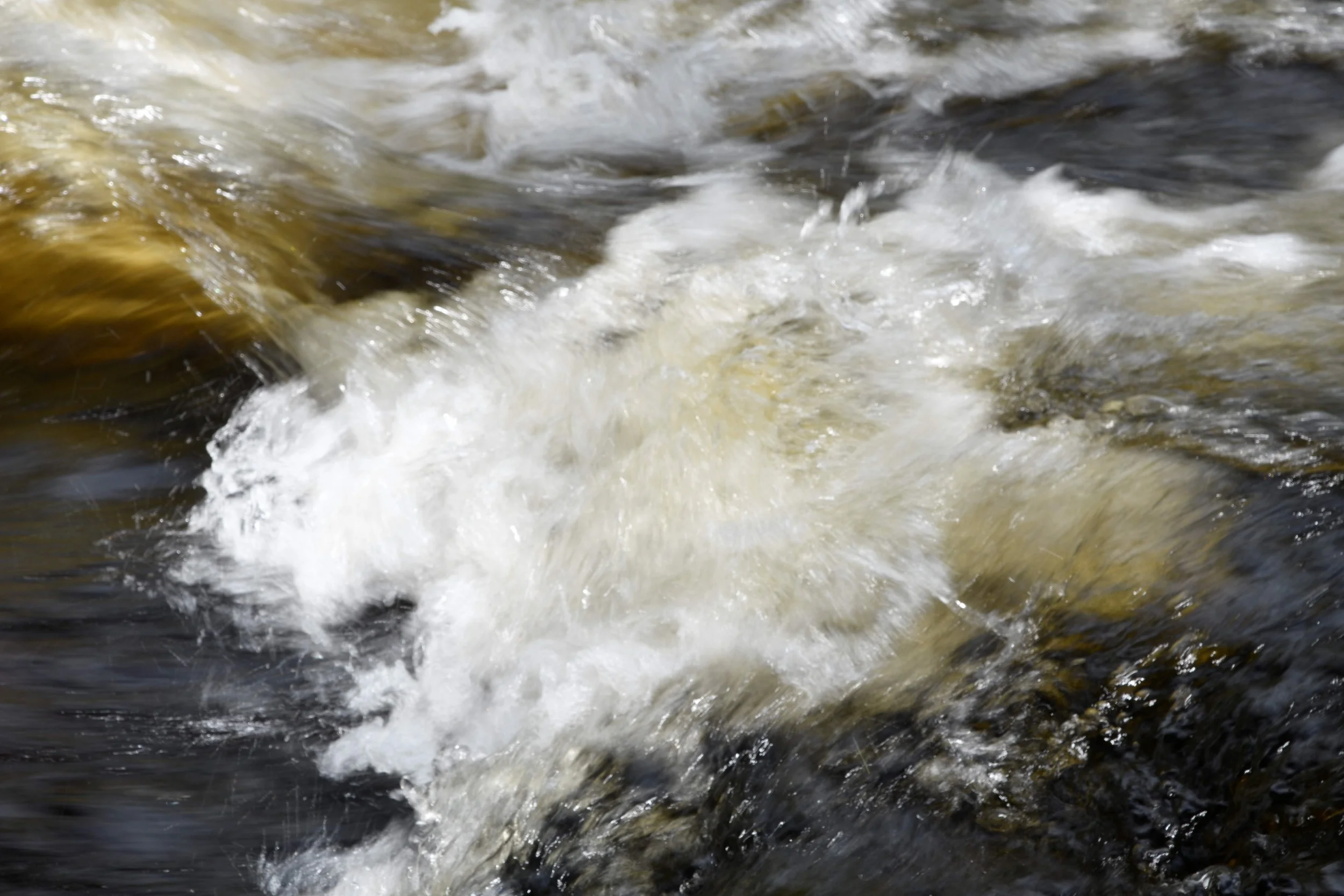 Flowing river water with white foam and dark rocks underneath.