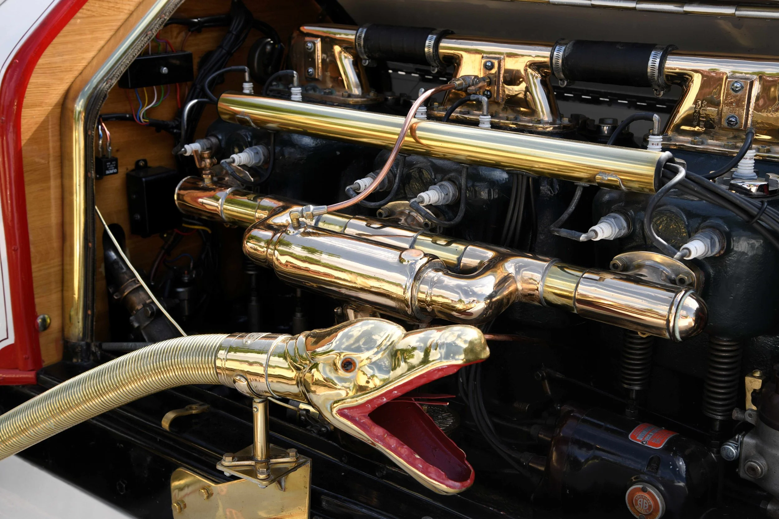 Close-up of an antique car engine with shiny gold and silver metal components, including pipes, wires, and mechanical parts.