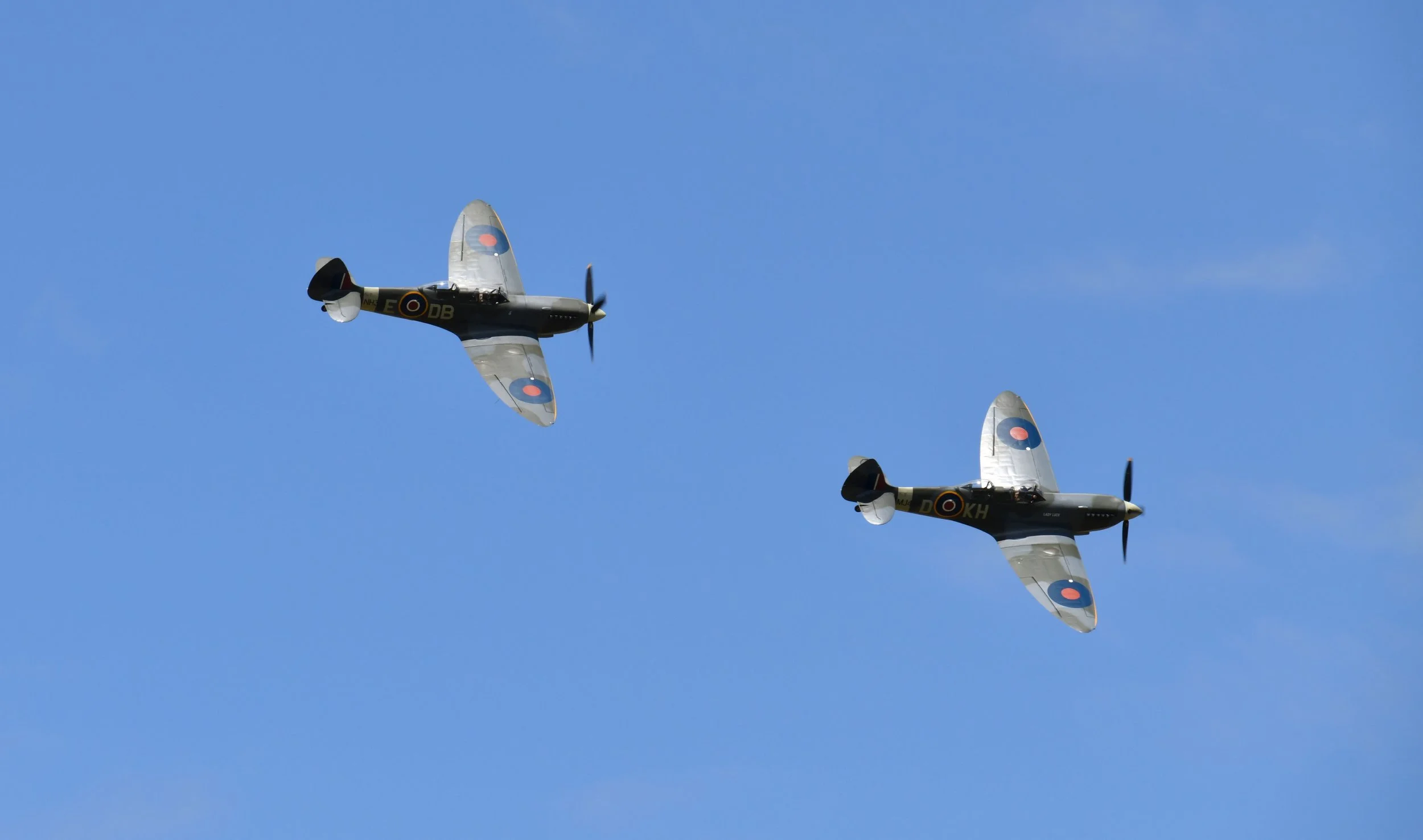 Two vintage military fighter planes flying in formation against a clear blue sky.