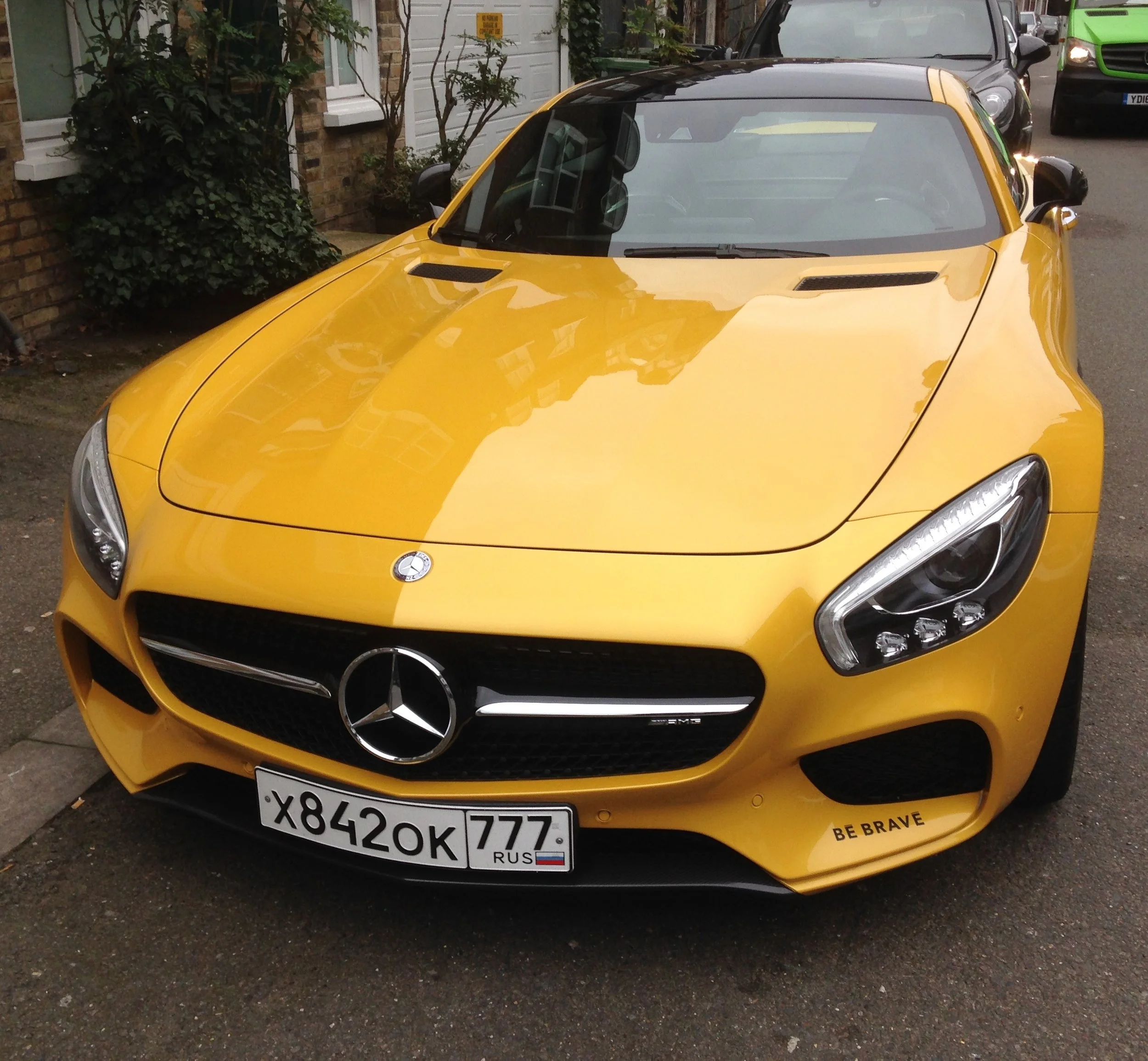 Yellow sports car parked on residential street, front view showing headlights, grille, and bumper, with license plate and black side mirrors.