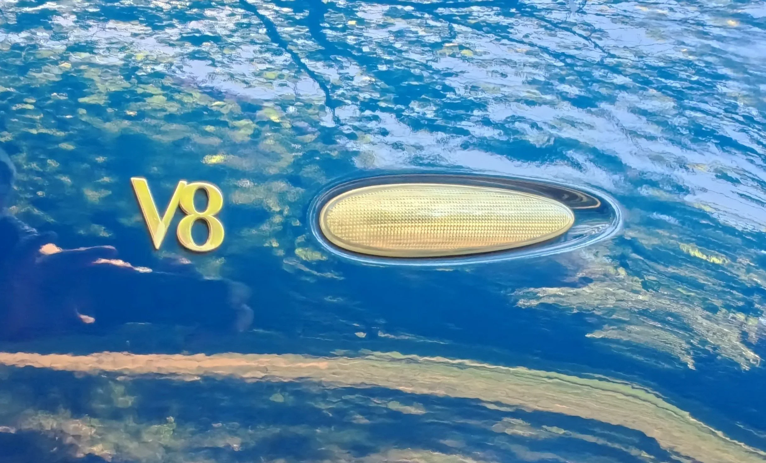 Close-up of a blue painted surface with a gold 'V8' emblem and a circular light fixture.
