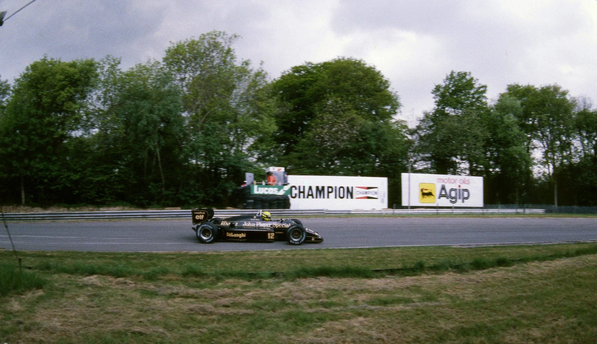 A black and gold Formula 1 race car driving on a race track, with trees and advertising signs in the background.
