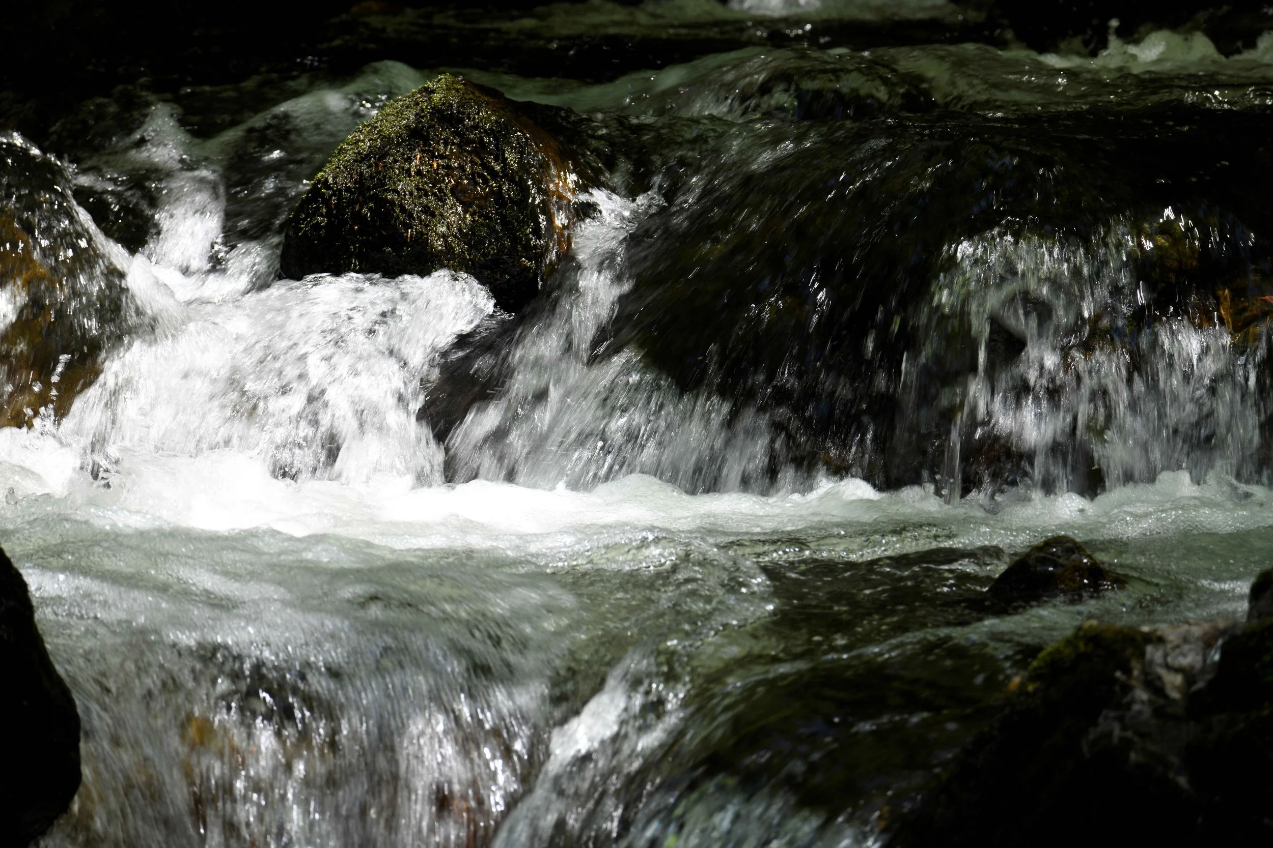 Flowing river water around rocks, some covered with moss, captured in motion.