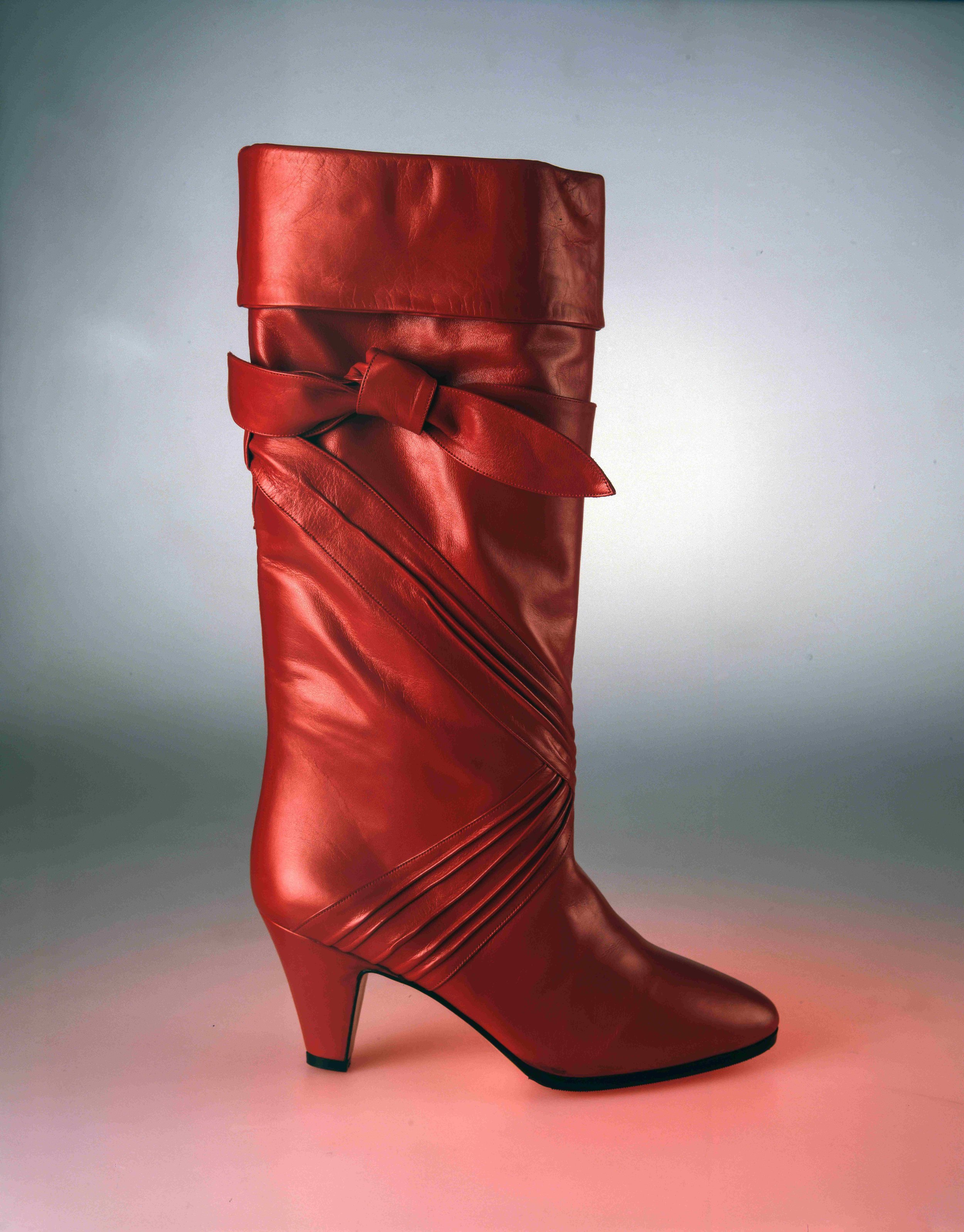 Red leather high-heeled boot with a bow detail around the ankle, set against a gradient background.