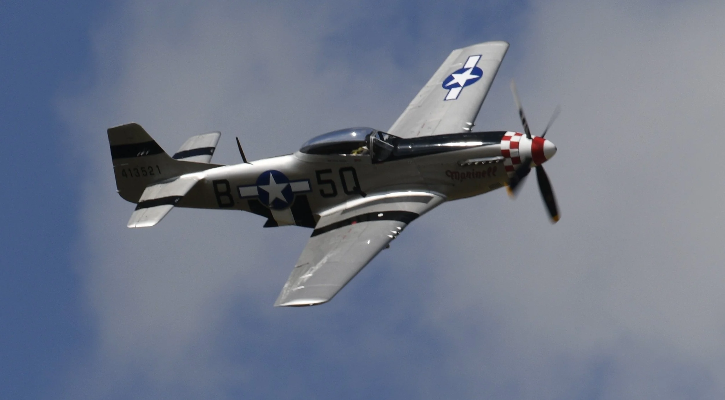 A vintage fighter airplane in flight against a blue sky with some clouds.