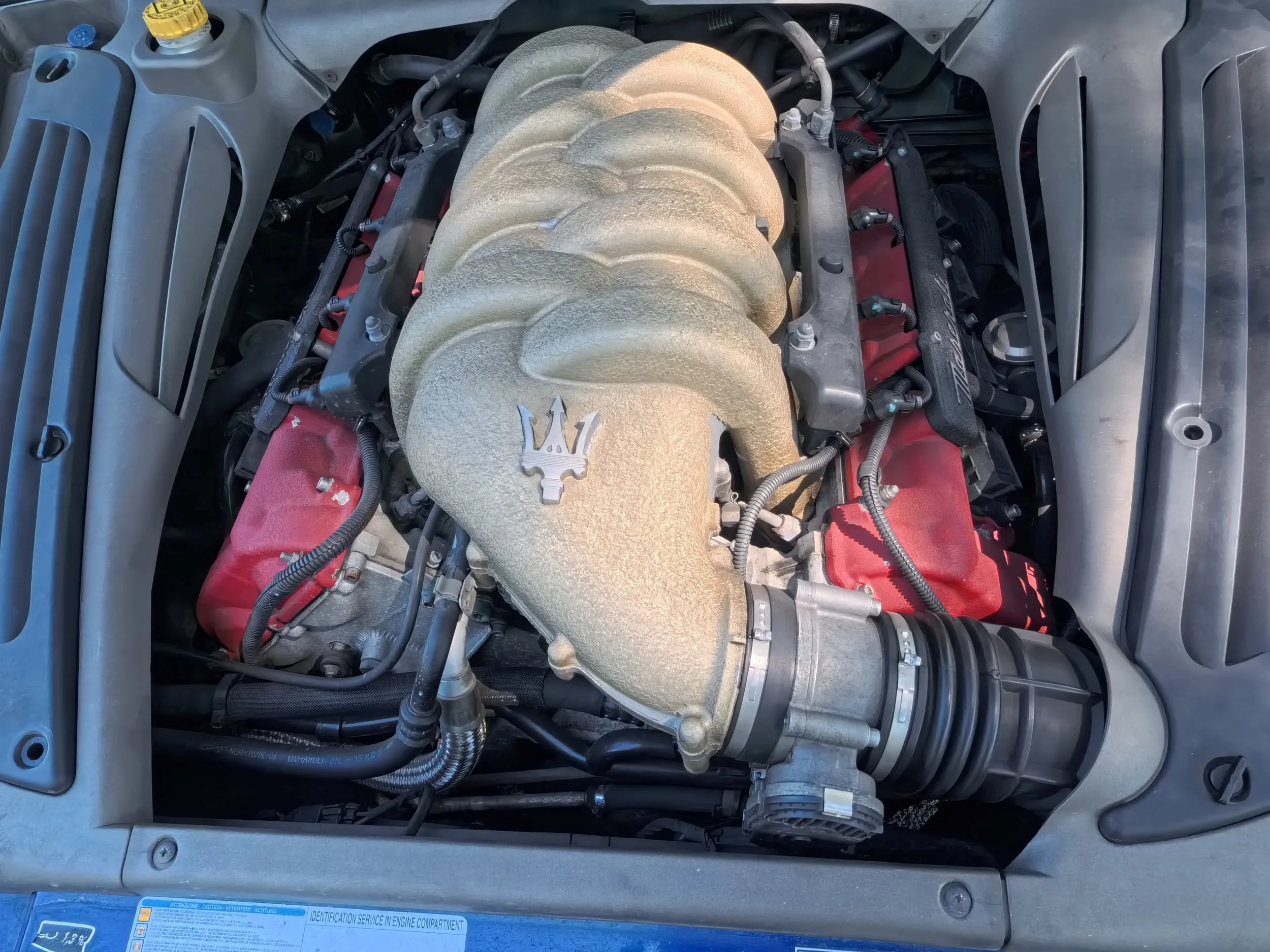 An engine compartment of a car showing the intake manifold, which is metallic with a textured surface, connected to various hoses and components.