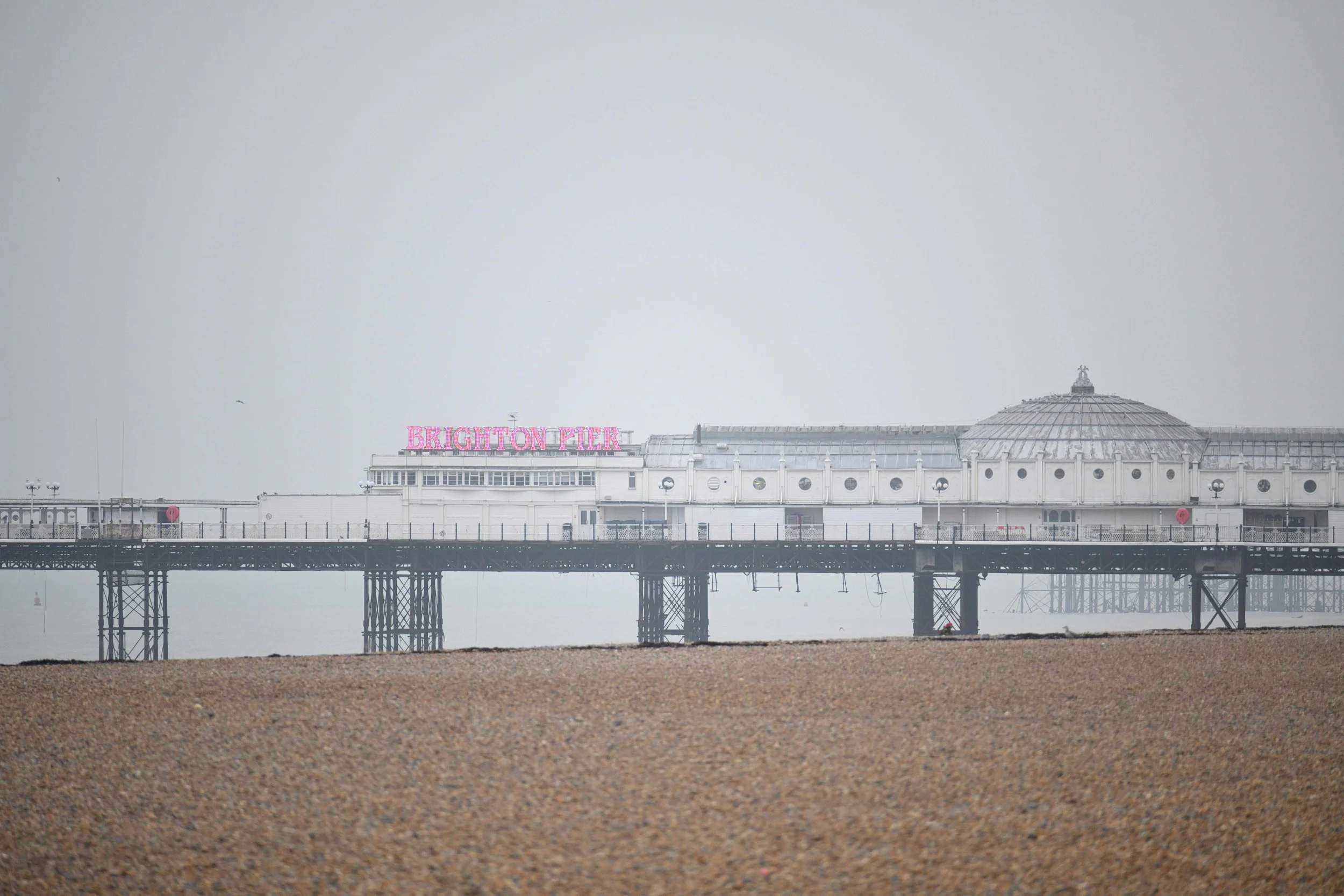 Image of Brighton Pier with a cloudy sky, an amusement park ride, and a sign that reads 'Brighton Pier' in pink letters.