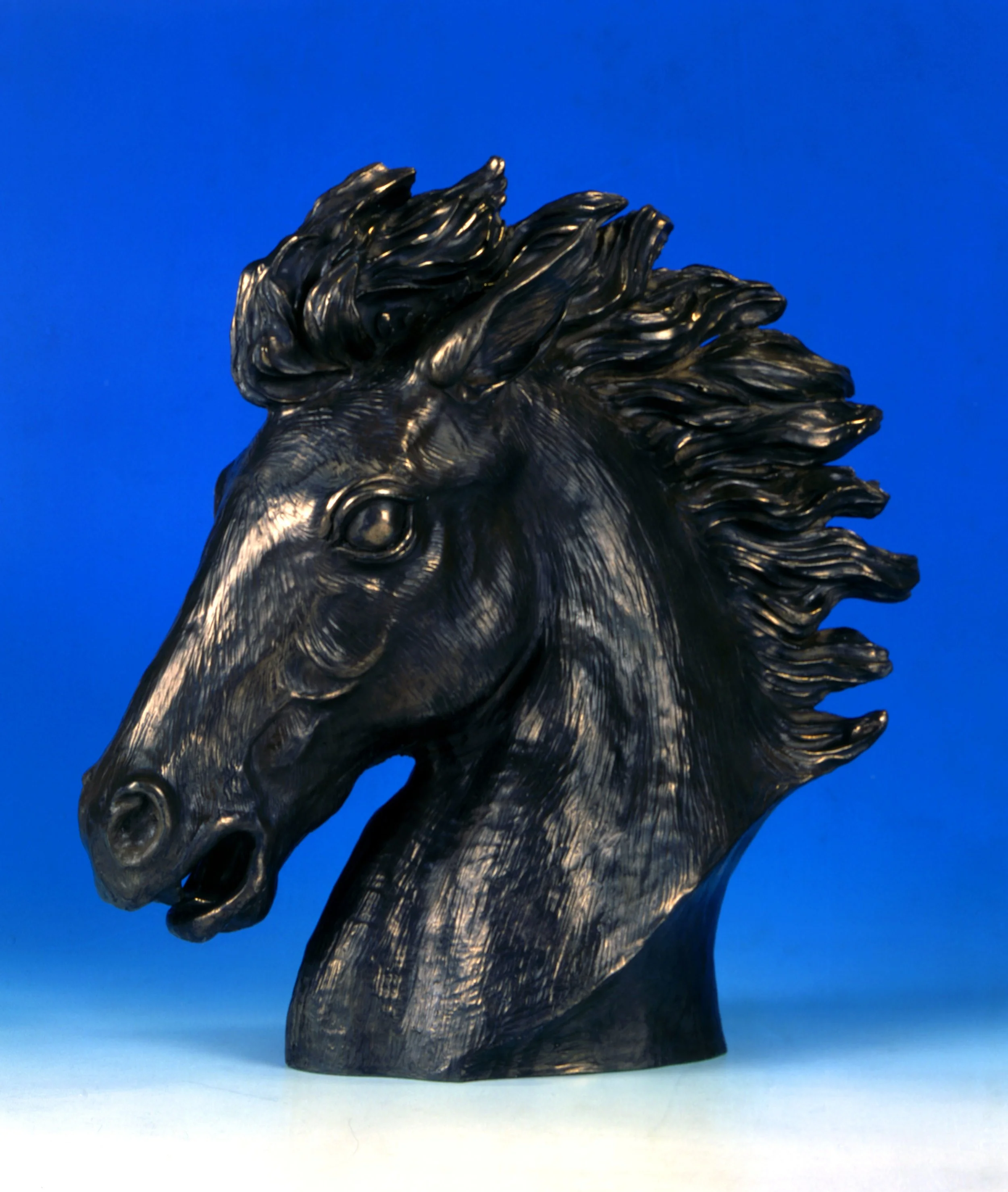 Close-up of a black metallic lion sculpture against a bright blue gradient background.