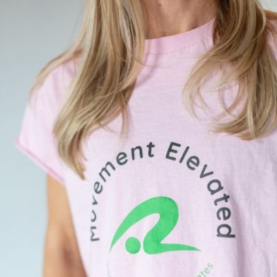 Close-up of a person wearing a light pink t-shirt with the words 'movement elevated' and a green logo.
