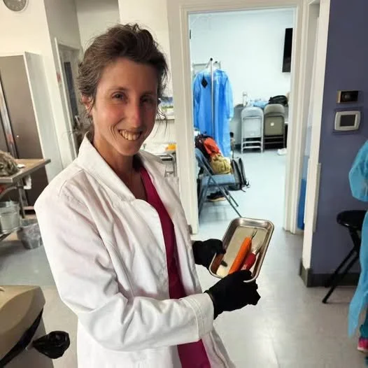A woman in a white lab coat holding a tray with a hot dog and a soda in a hospital or healthcare setting.