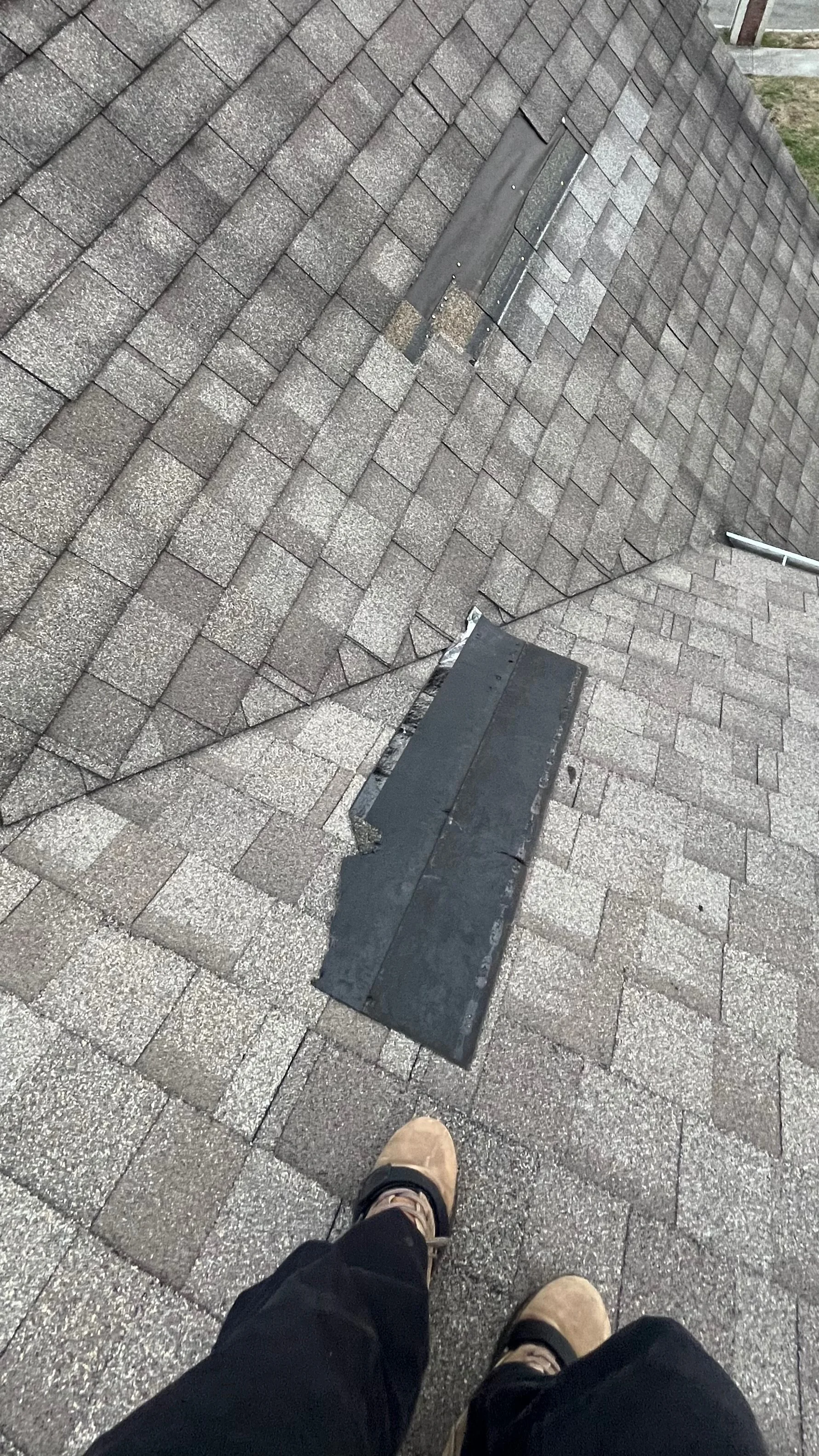 Photo taken from a rooftop showing shingles and HVAC vents, with a person's feet visible in the foreground.