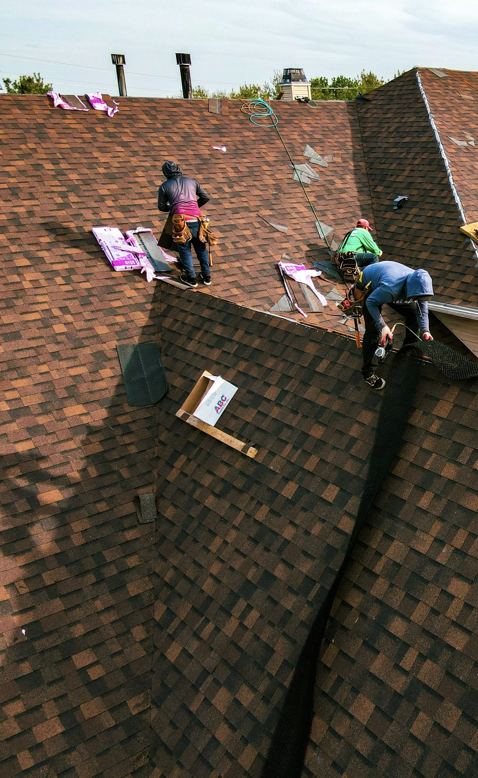 Construction workers installing shingles on a house roof.