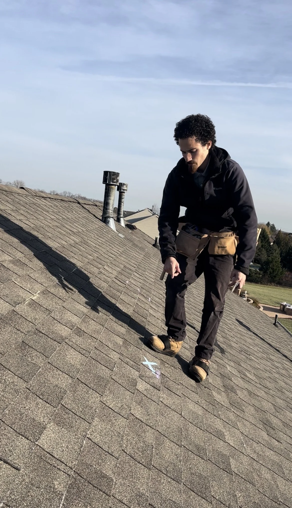 A man inspecting a shingle roof with chalk markings during daytime.