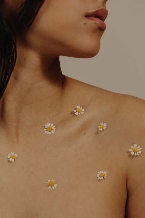Close-up of a woman's bare shoulder and neck with small daisy flower stickers on her skin.