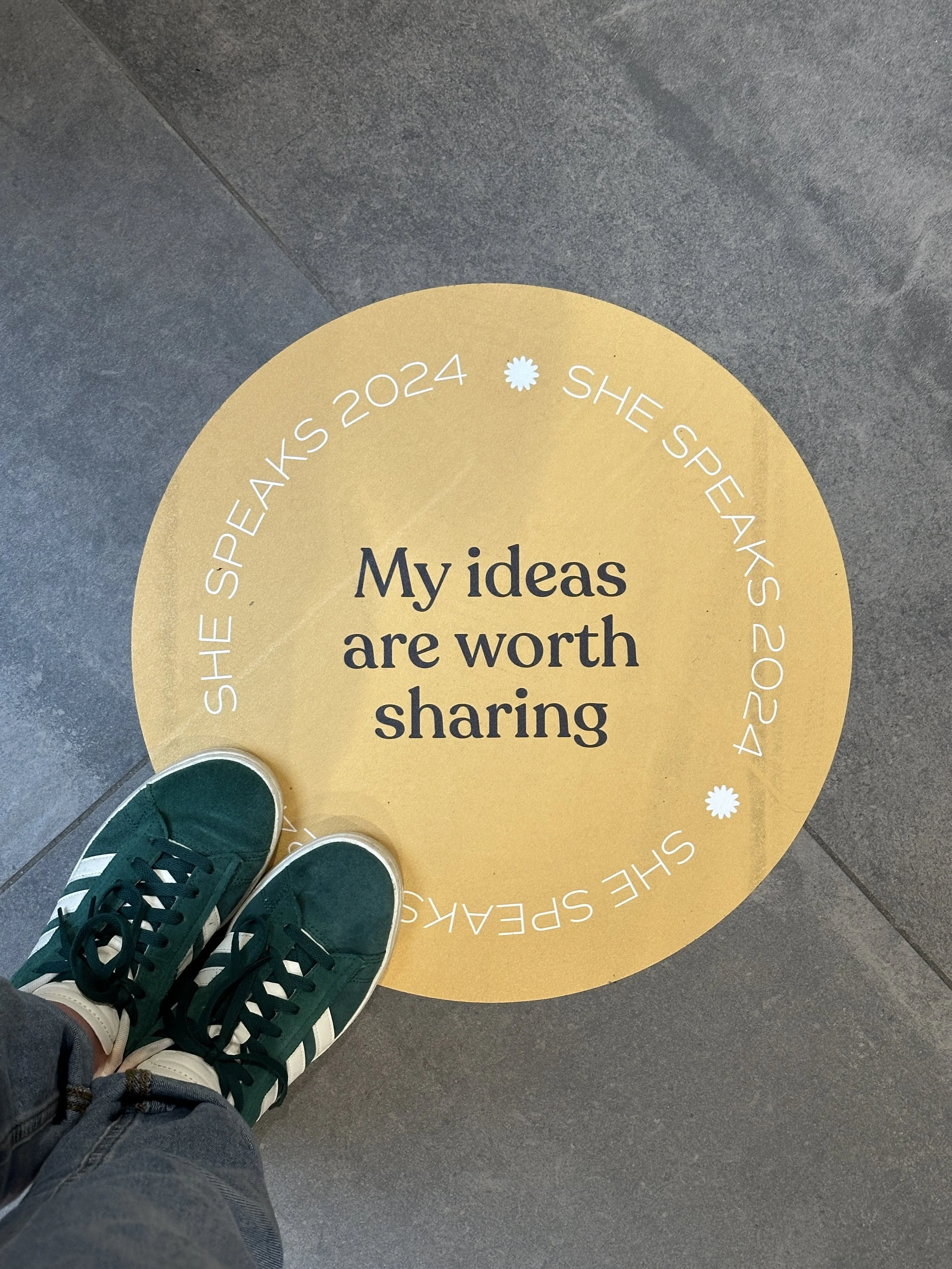 Floor sticker with the message "My ideas are worth sharing" surrounded by a circle of smaller text "SHE SPEAKS 2024" with a mulitflower symbol in the circle