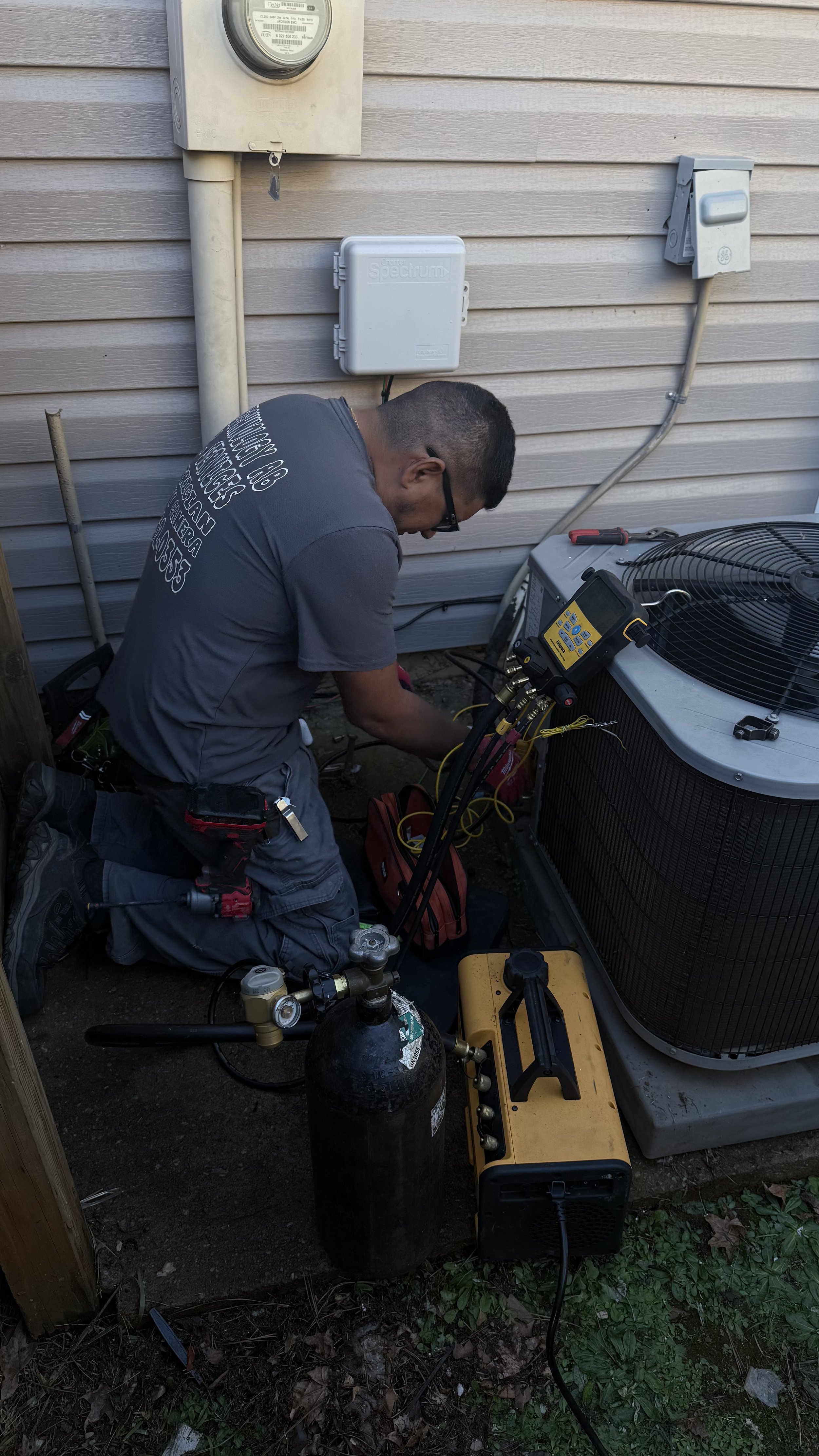 A technician servicing an outdoor air conditioning unit with tools and gauges.
