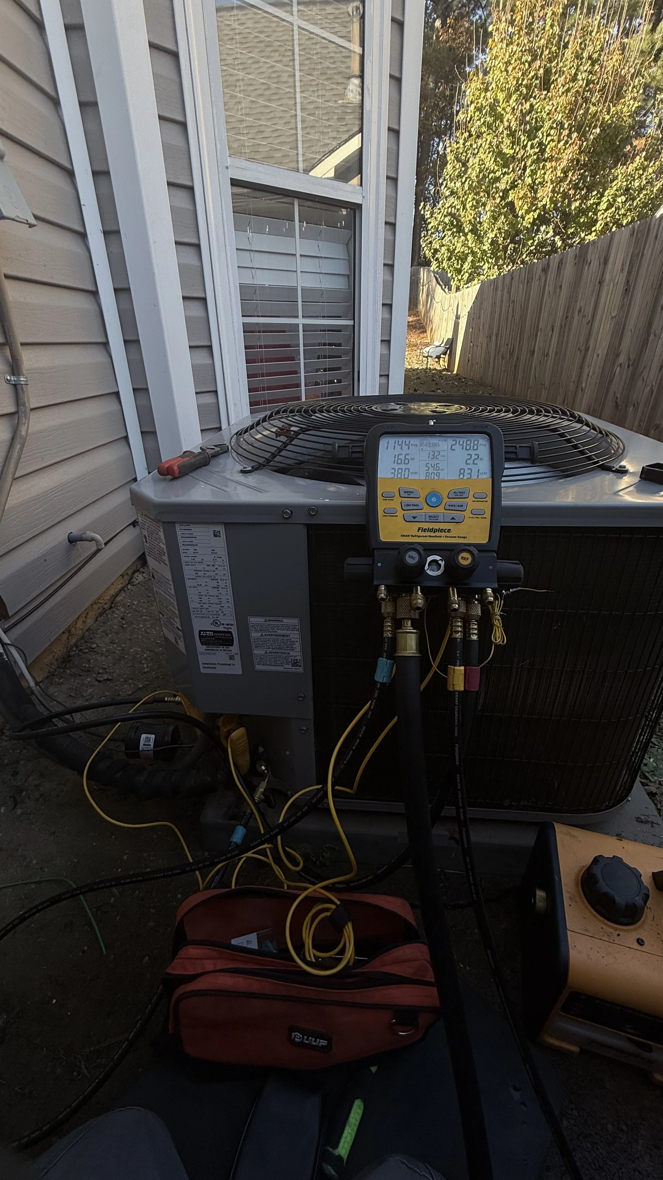 An outdoor air conditioning unit with a digital thermometer and HVAC tools resting on top and nearby.