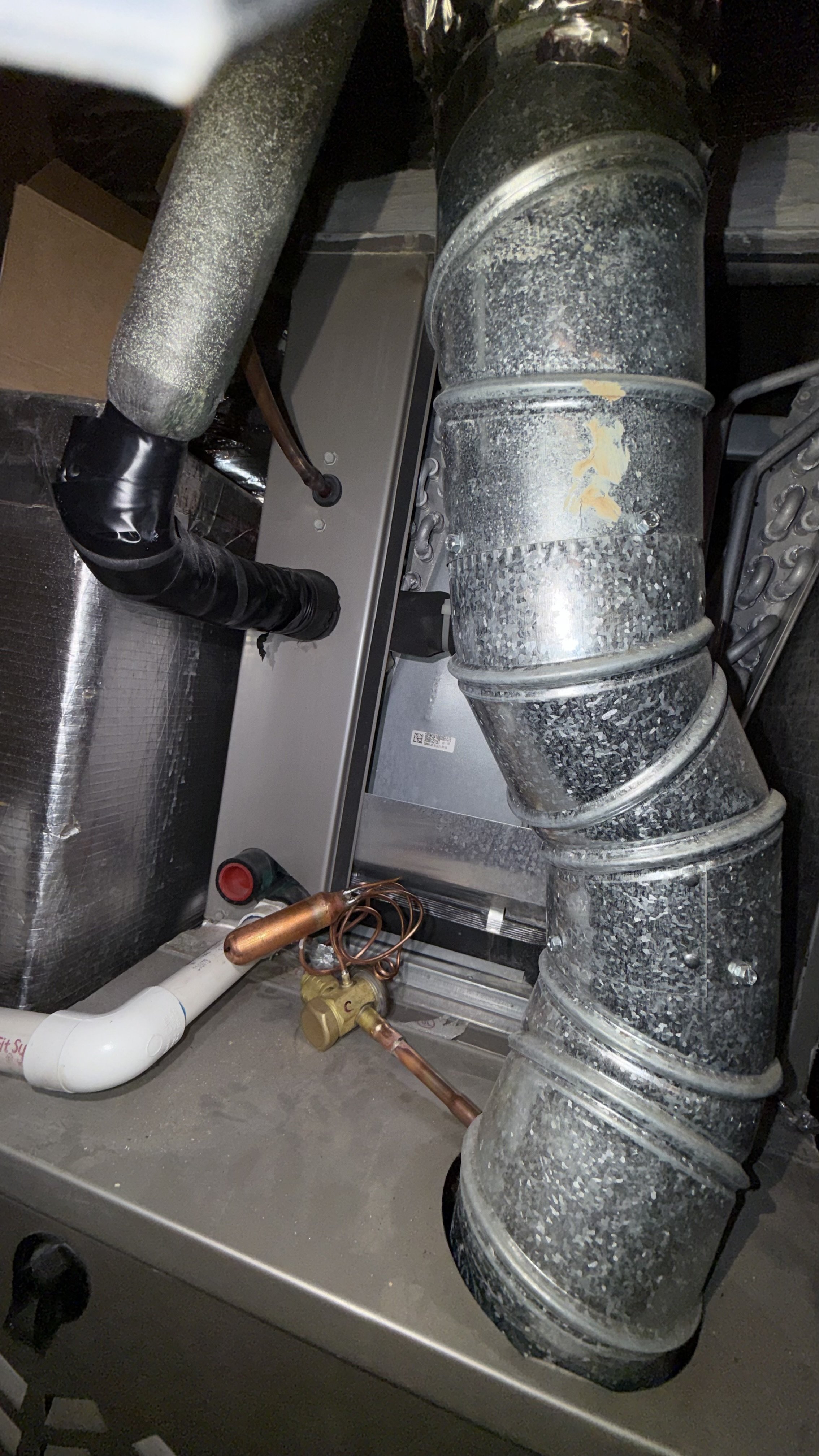 A close-up photo of HVAC ductwork and components, including metal ducts, copper pipes, and insulation material.