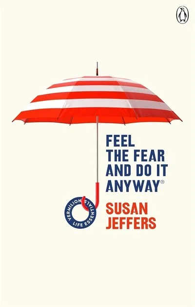A red and white striped umbrella with the text "Feel the Fear and Do It Anyway" and the author name "Susan Jeffers" below it.