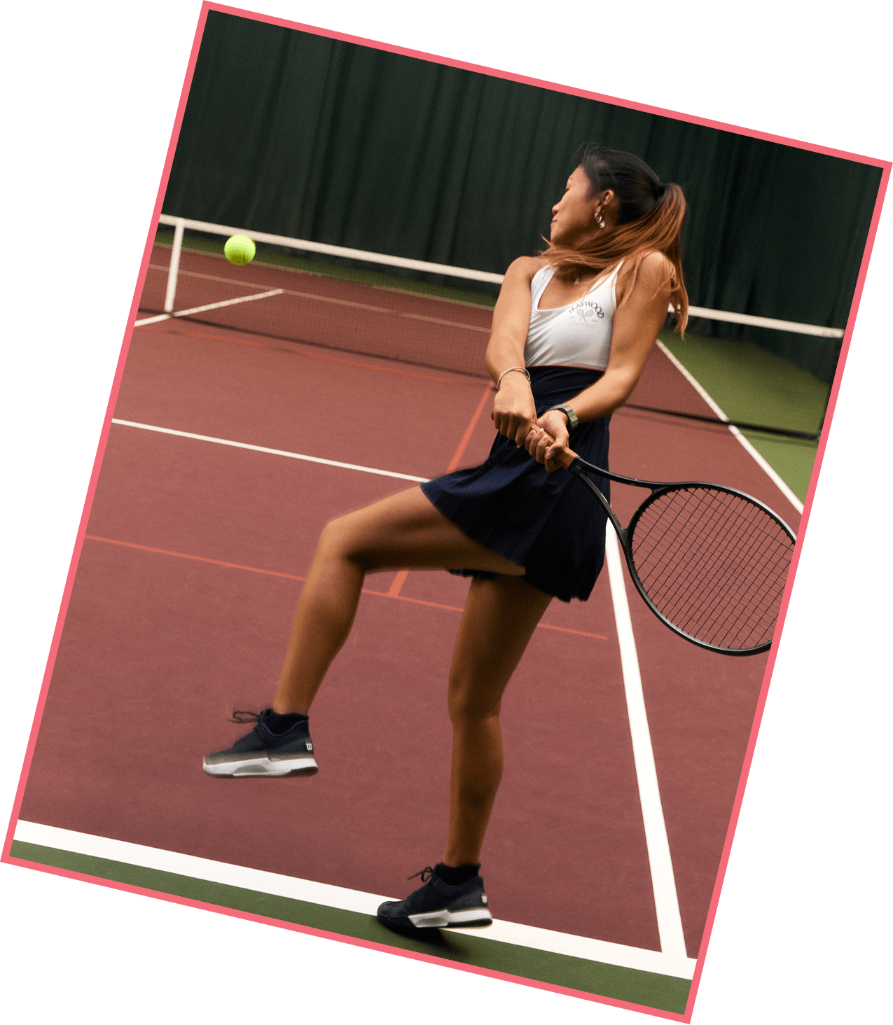 Woman playing tennis on an indoor court, preparing to hit the ball with her racket.