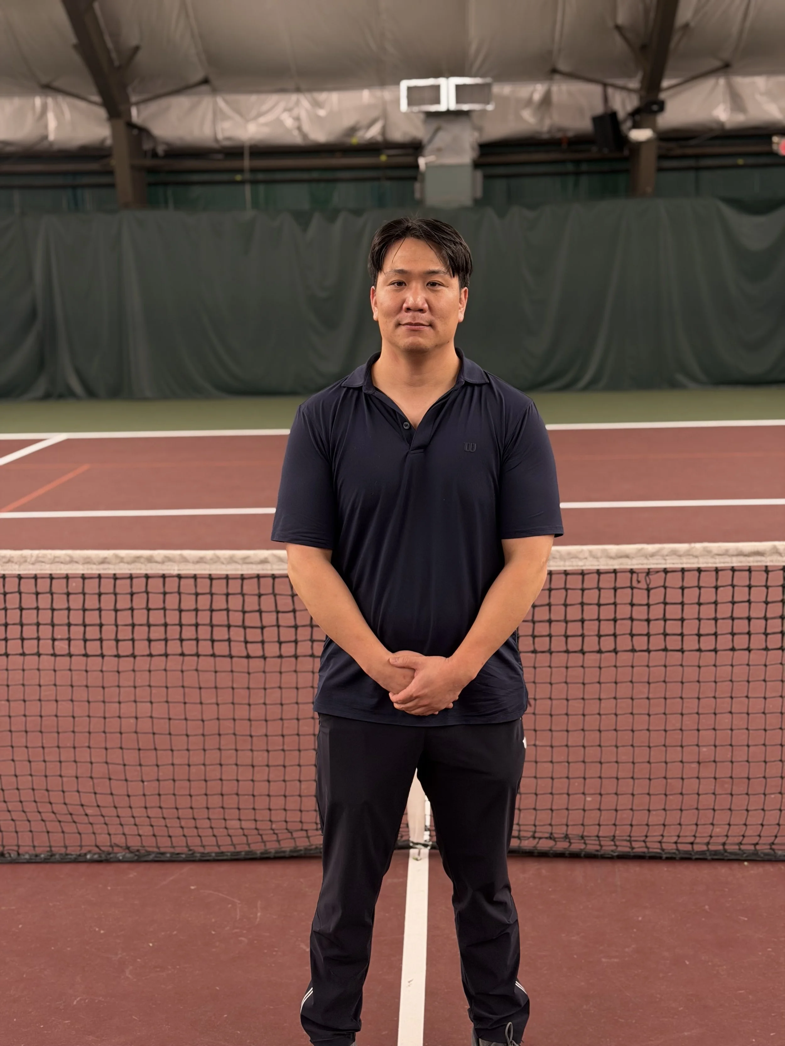 A man standing on an indoor tennis court with a net in front of him.
