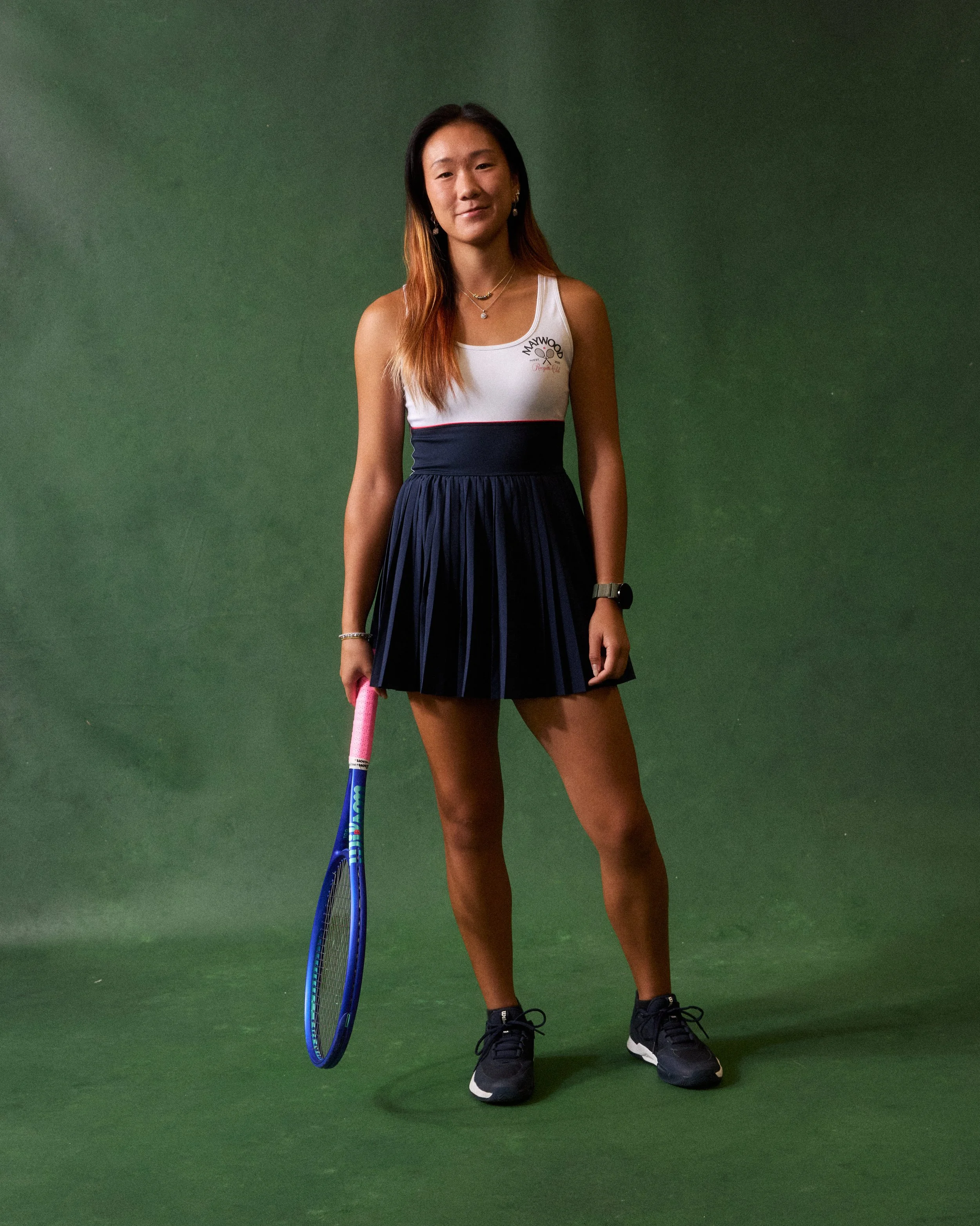Young woman holding a tennis racket standing on a green backdrop.