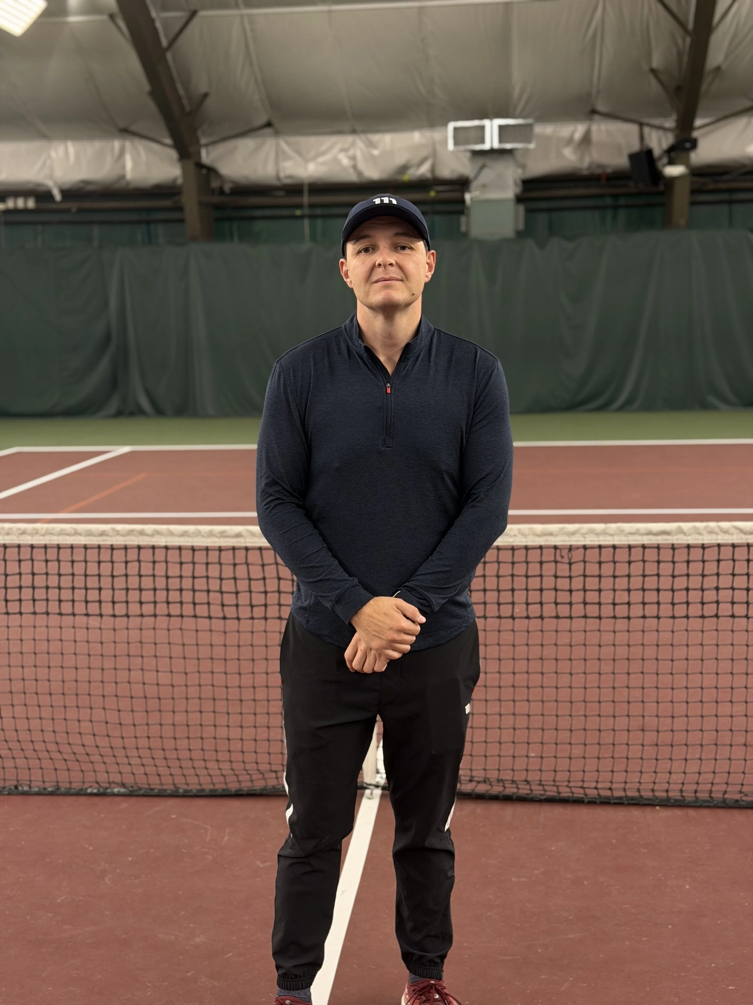 A man in athletic wear standing on an indoor tennis court behind a net.