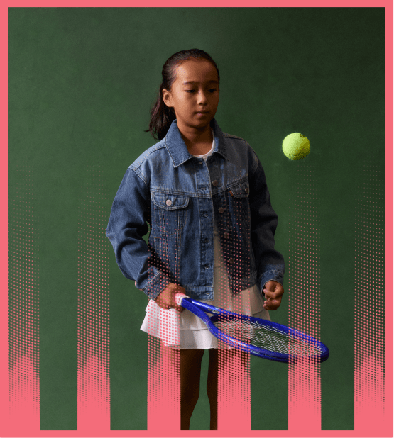 Young girl in a denim jacket playing tennis with a green tennis ball in mid-air.