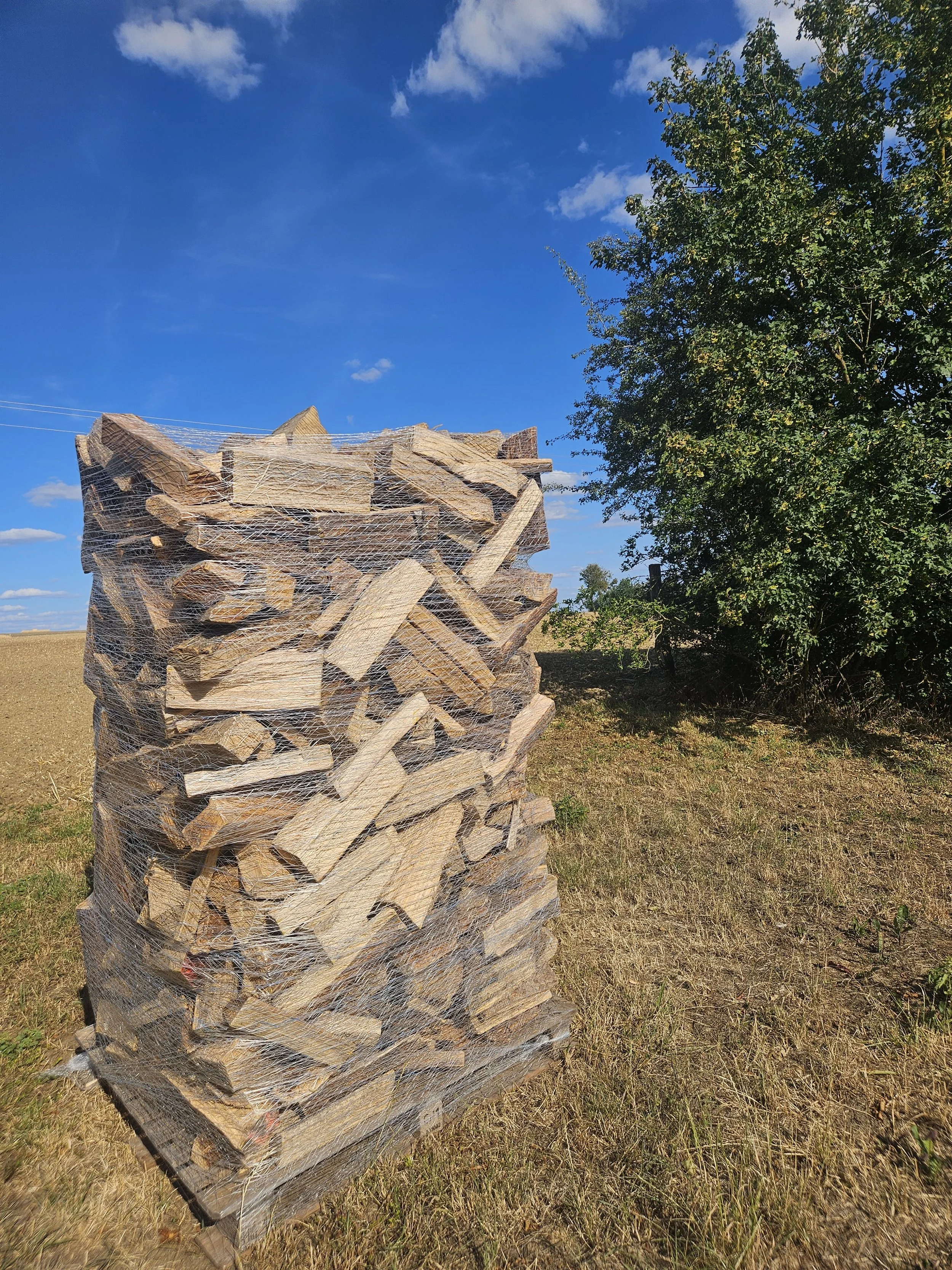 Explosé de bois dans une structure en filet totalement blanc, situé dans un champ avec des arbres et un ciel bleu avec quelques nuages.