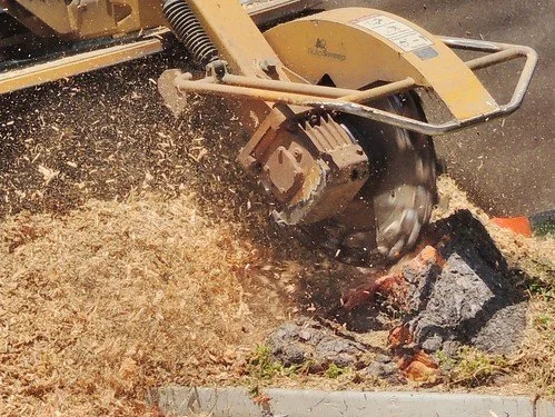 A yellow concrete saw cutting through a concrete block, creating dust and debris.