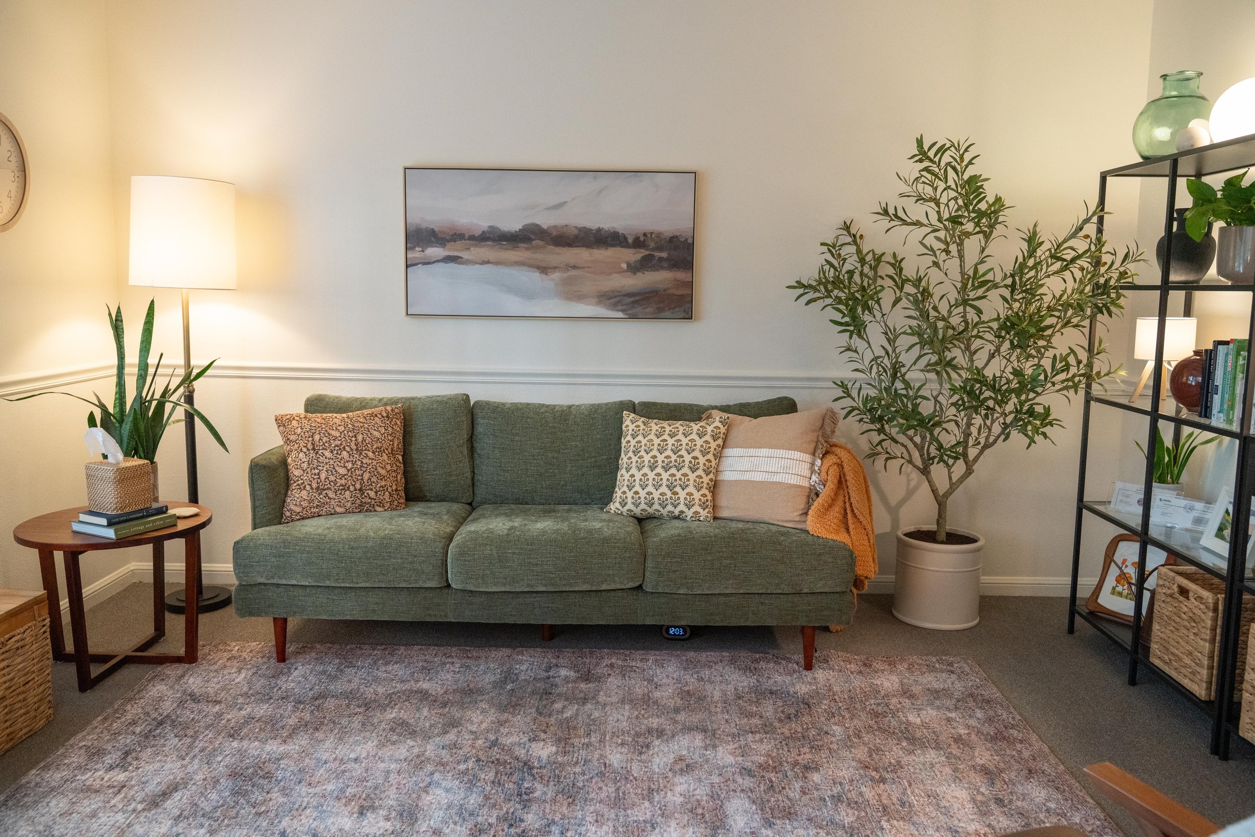 Living room with green sofa, artwork, potted plant, bookshelf, and various decor items.