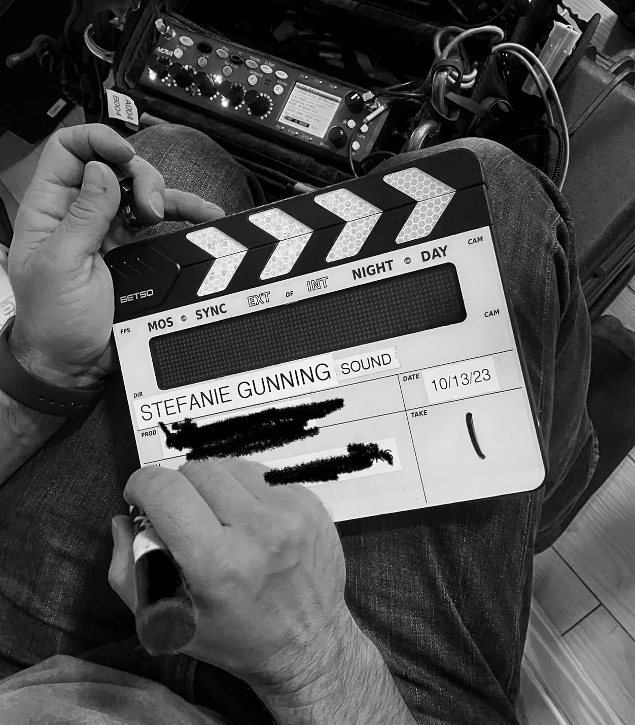 A person holding a clapperboard with the name 'Stefanie Gunning Sound' written on it, sitting in front of audio equipment with various controls and cables.