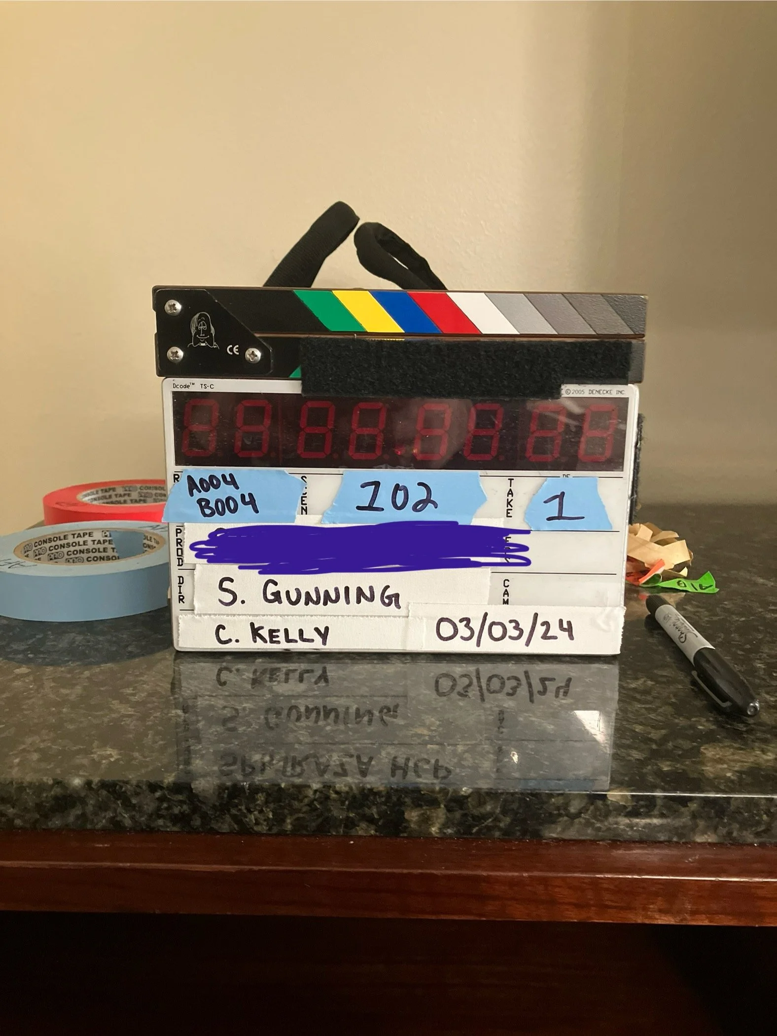 Clapperboard with handwritten notes, tape, marker, and some small clips on a countertop