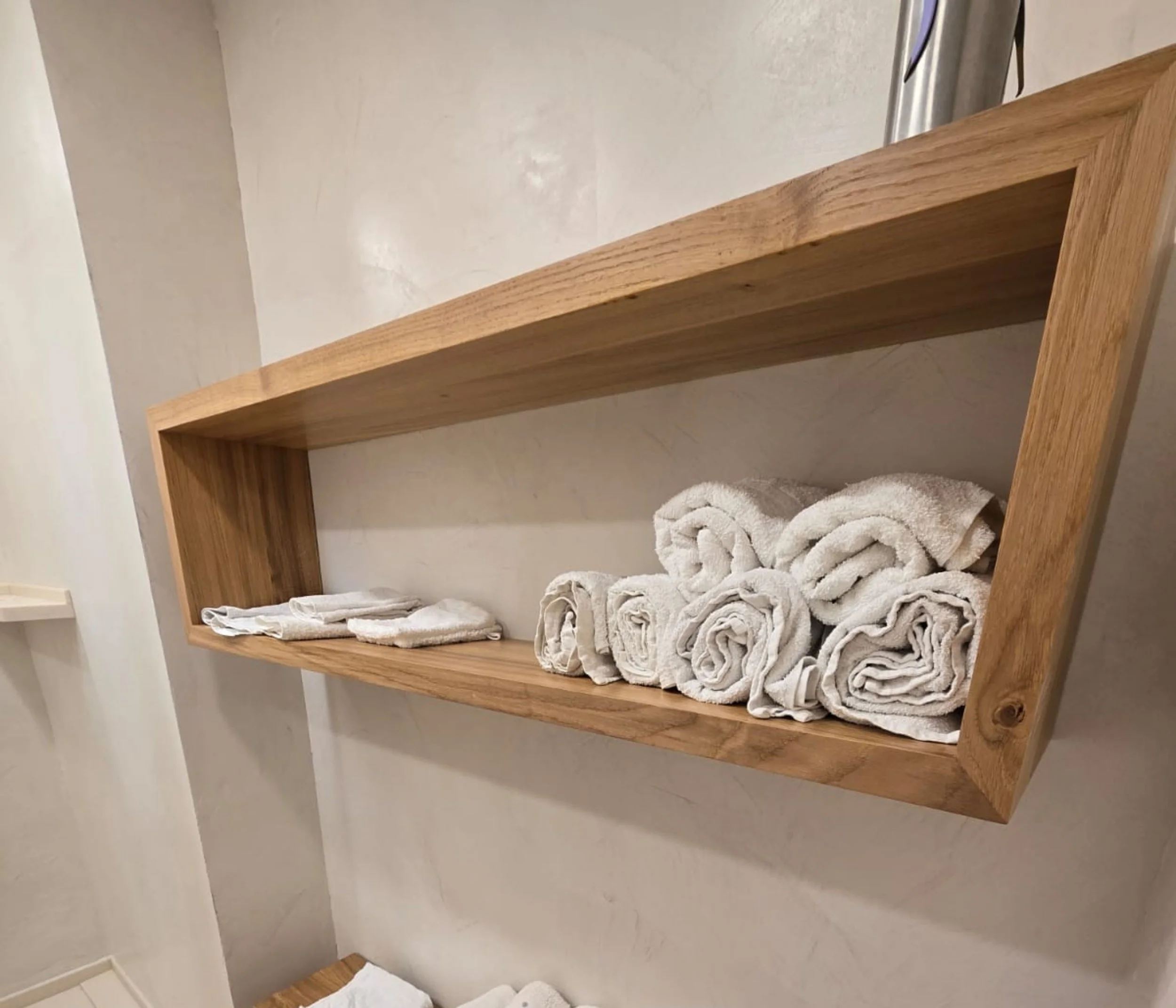 Étagère en bois fixée au mur, avec des serviettes blanches roulées posées dessus.