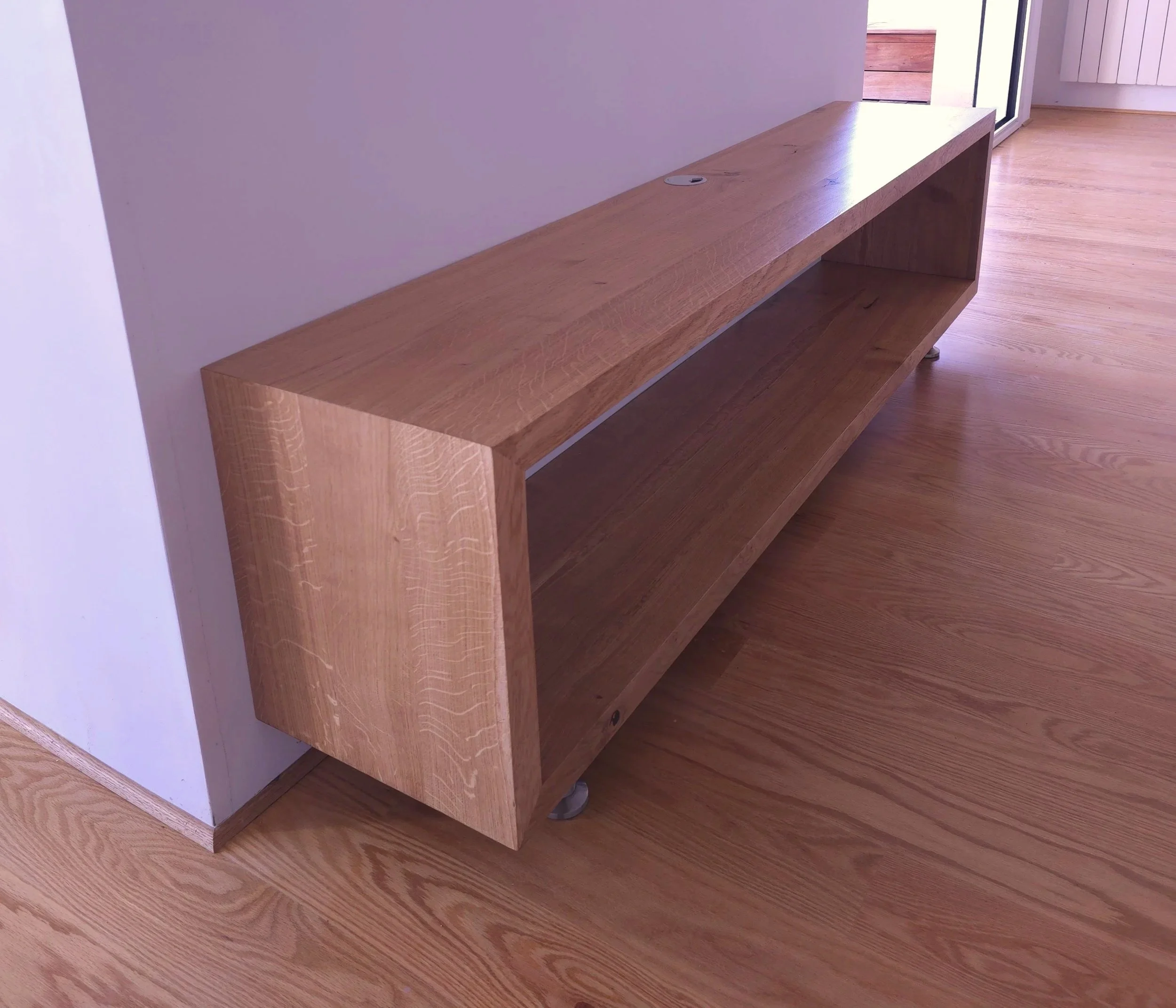 meuble tv sur mesure en bois clair dans une pièce moderne, posé contre un mur blanc, avec un sol en bois assorti.