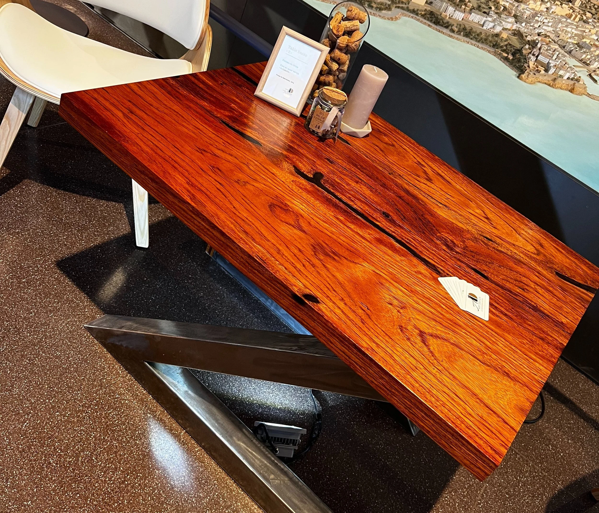 Table en bois massif avec une surface polie, décorée avec un cadre, une bougie, et un pot de gelée, sur un fond de mur avec une carte de ville