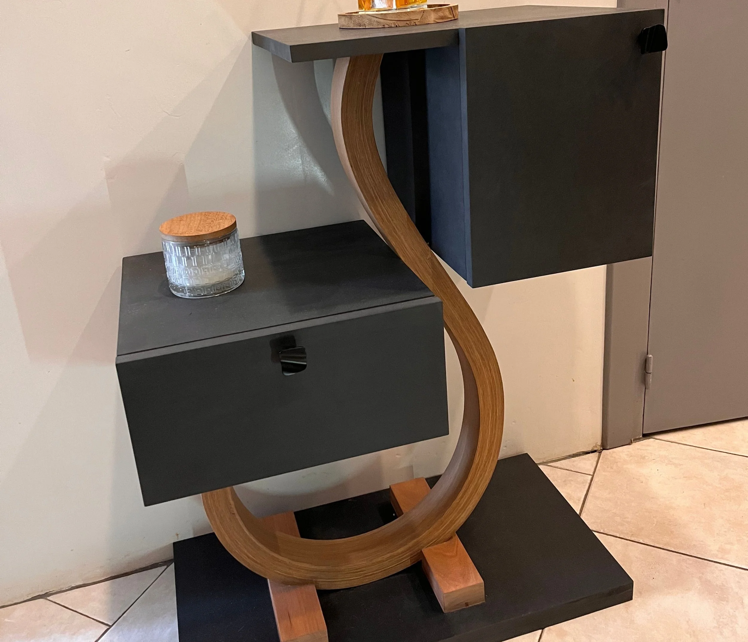 Meuble d'angle moderne en bois et en noir avec un tiroir et une étagère, décoré d'une bougie dans un pot en verre et en bois.