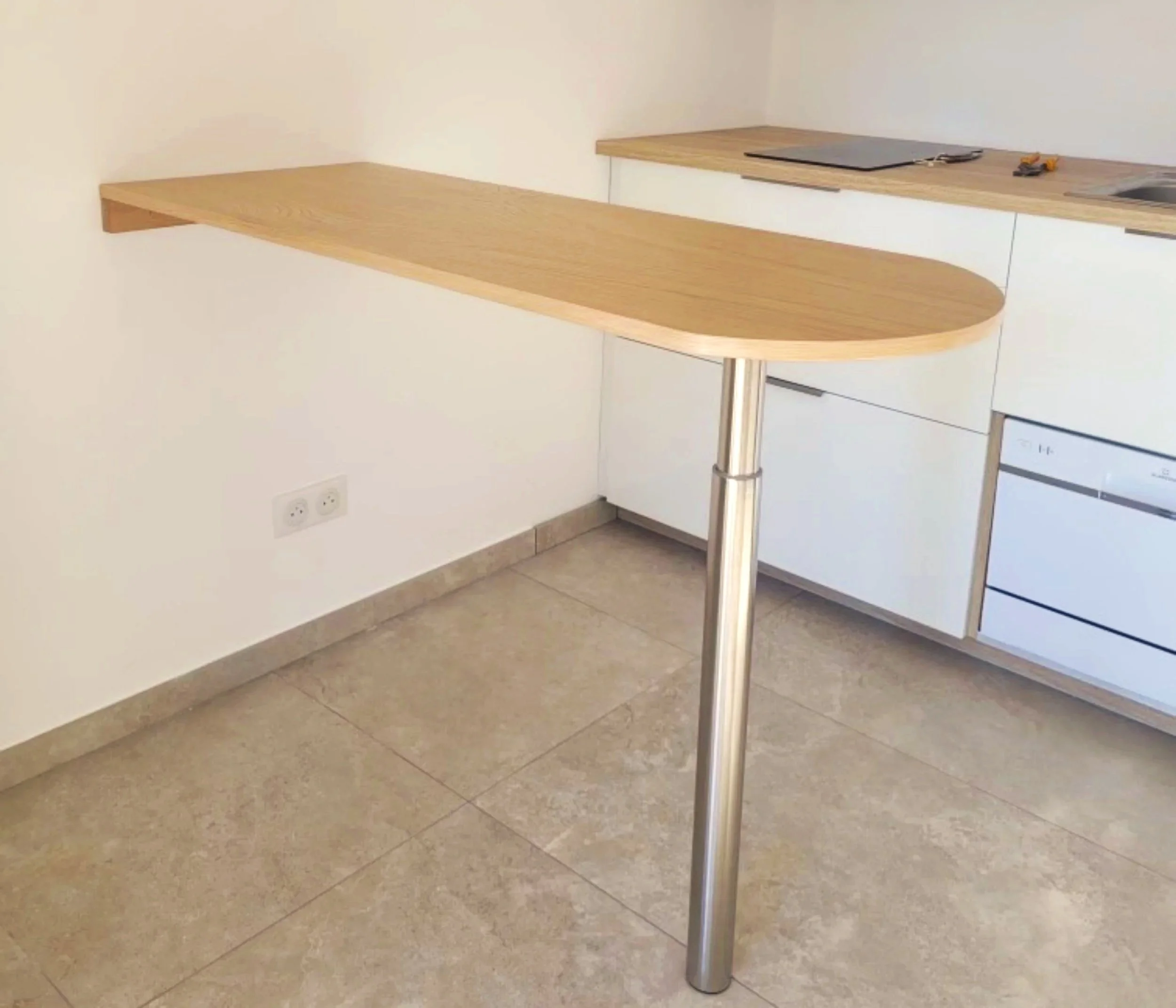 Un comptoir de cuisine en bois arrondi soutenu par un seul pied en métal dans une cuisine moderne.